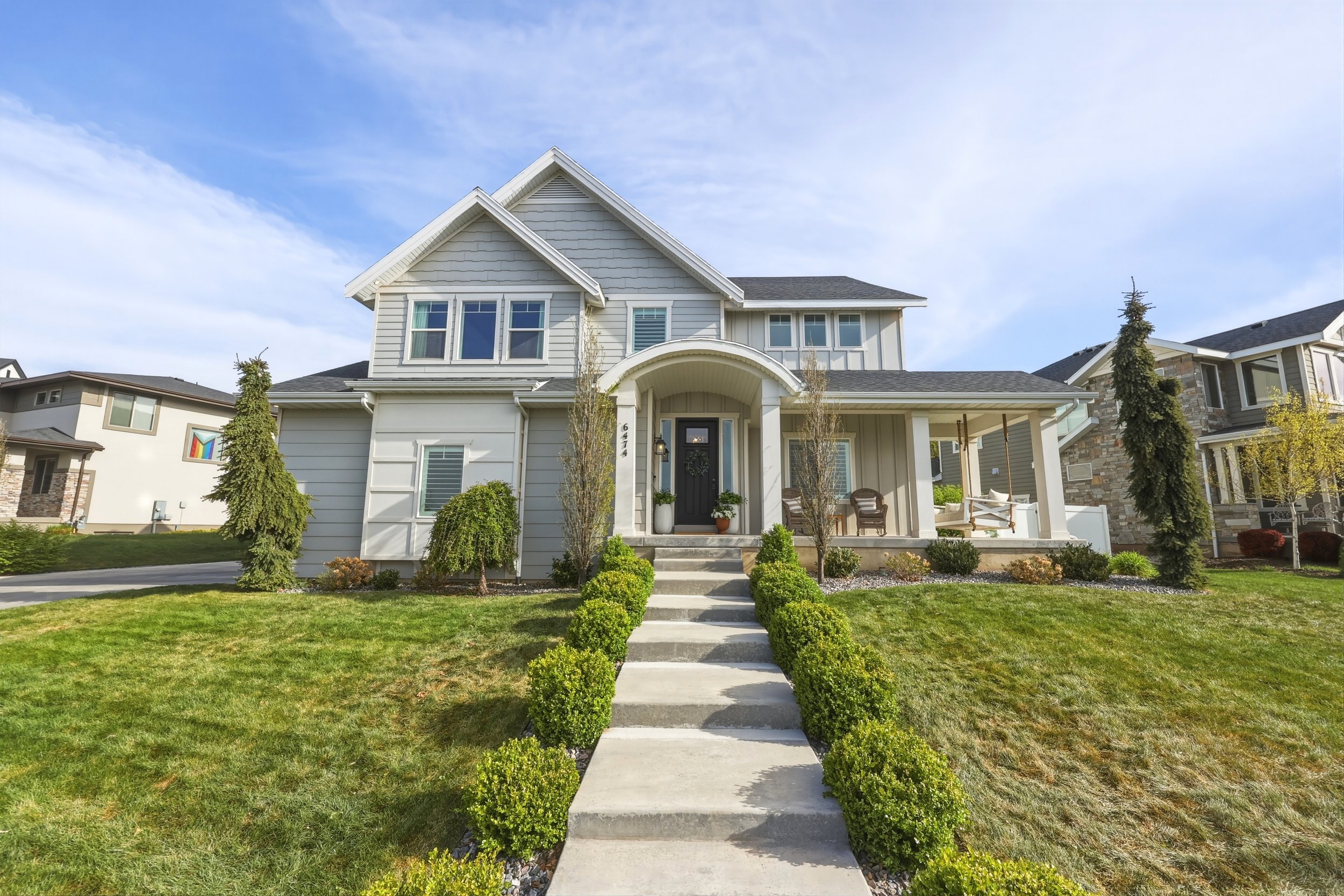 Front view of a two-story white house with a front porch, steps, green lawn, and small shrubs, under a partly cloudy sky.