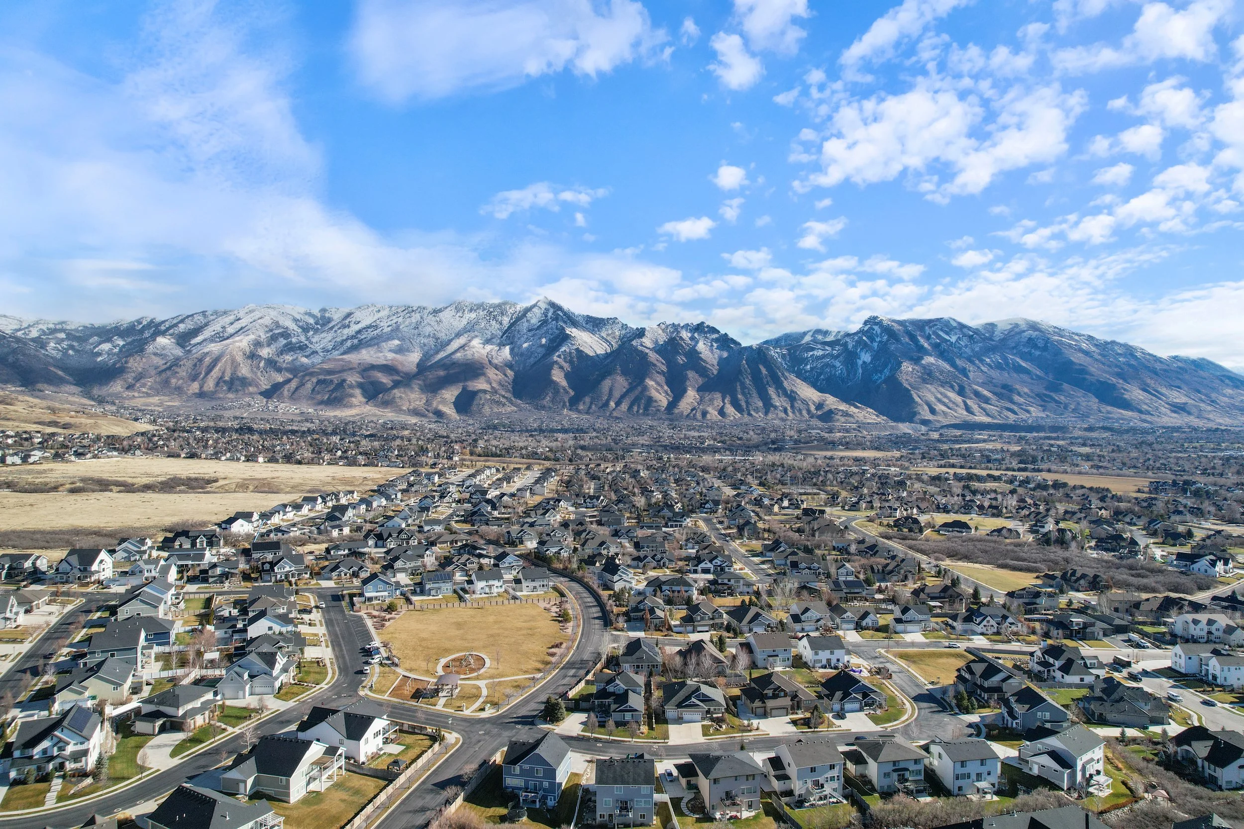 A residential neighborhood with a mountain range in the background and a partly cloudy blue sky.