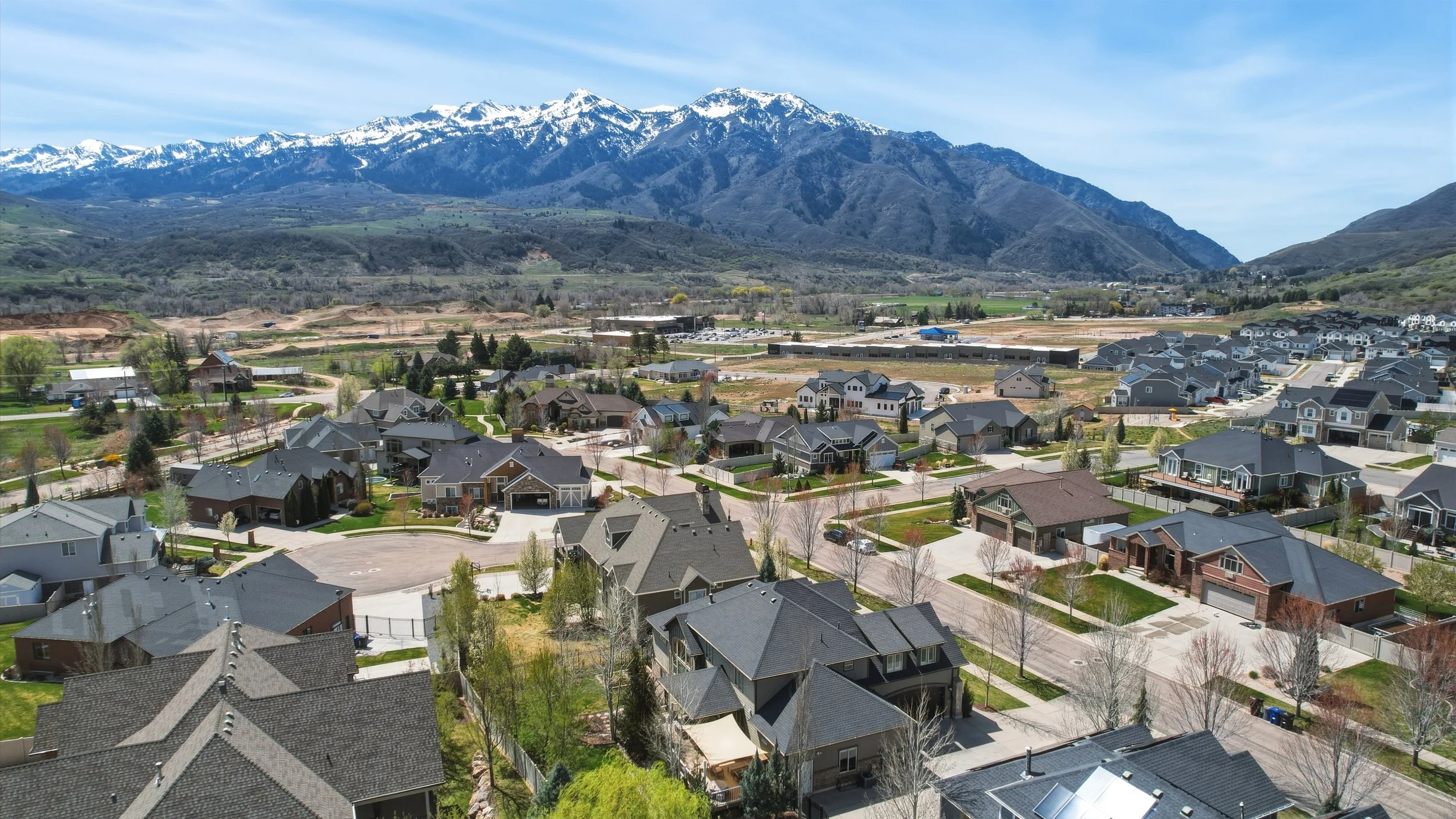 A residential neighborhood with houses and streets at the base of a mountain range with snow-capped peaks.