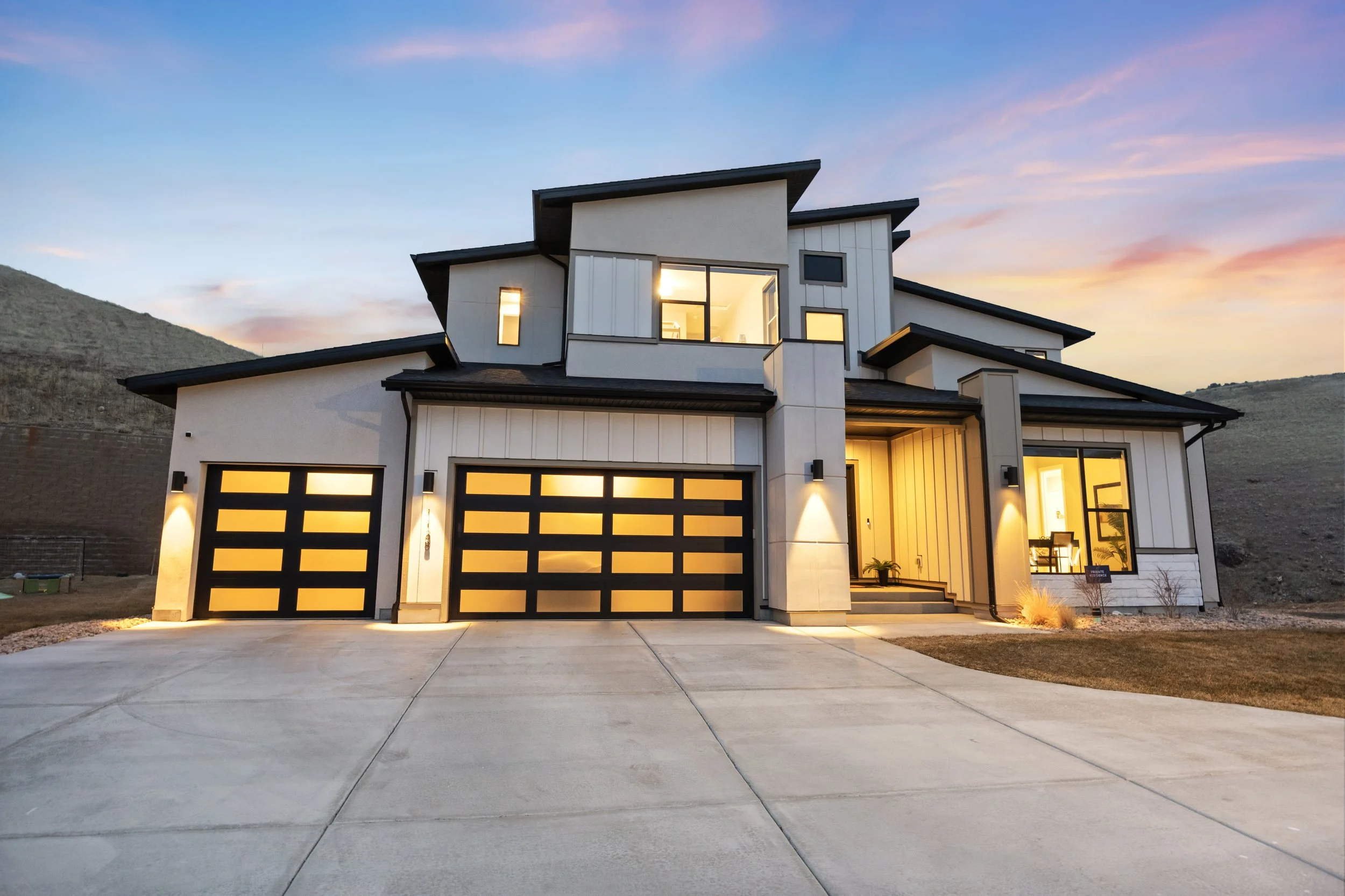Modern luxury home in Draper, Utah near Point of the Mountain photographed at sunset with illuminated garage doors and mountain views.