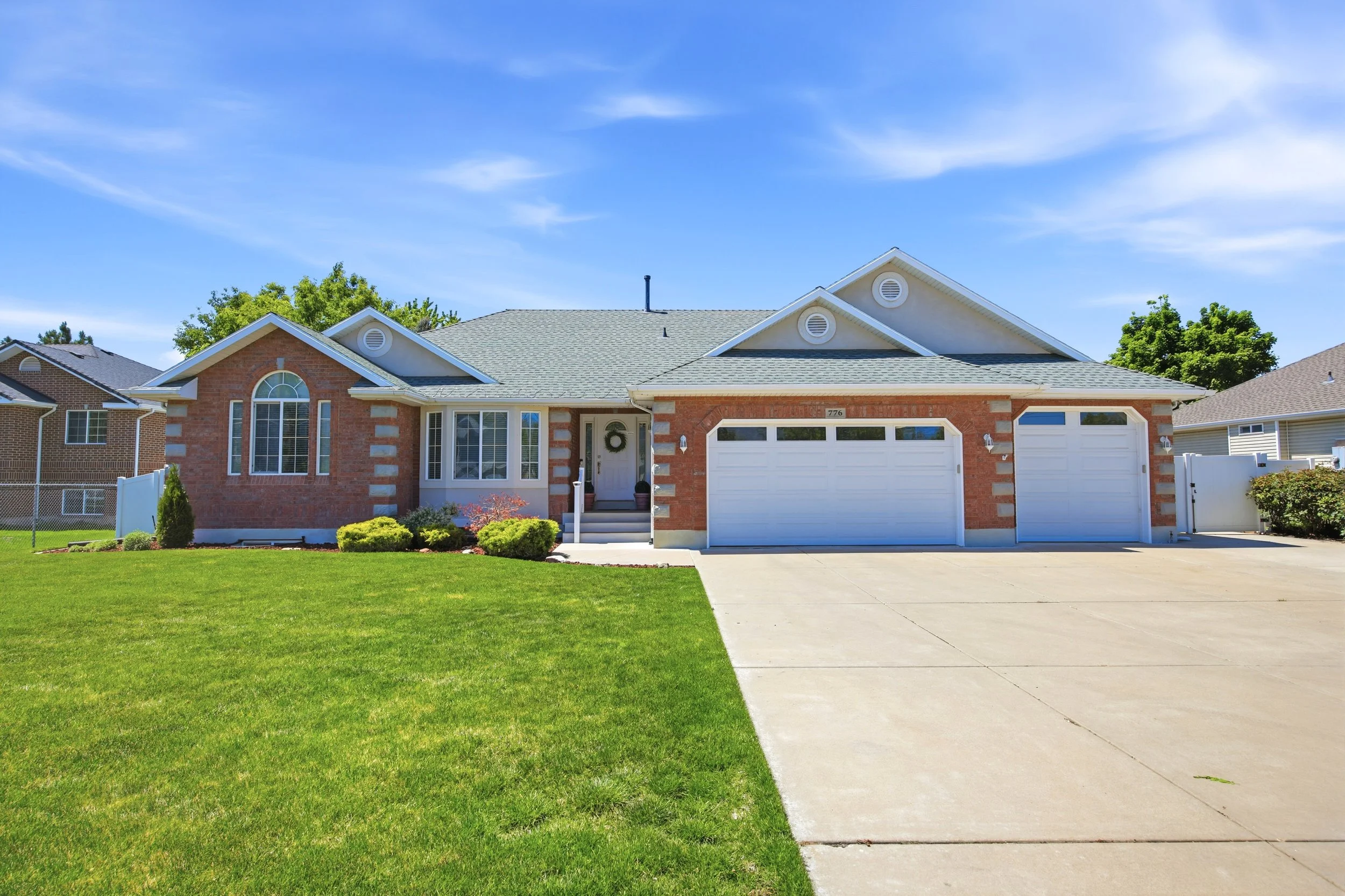 Front view of a two-story brick house with white garage doors, a walkway, and a lawn under a blue sky with some clouds.
