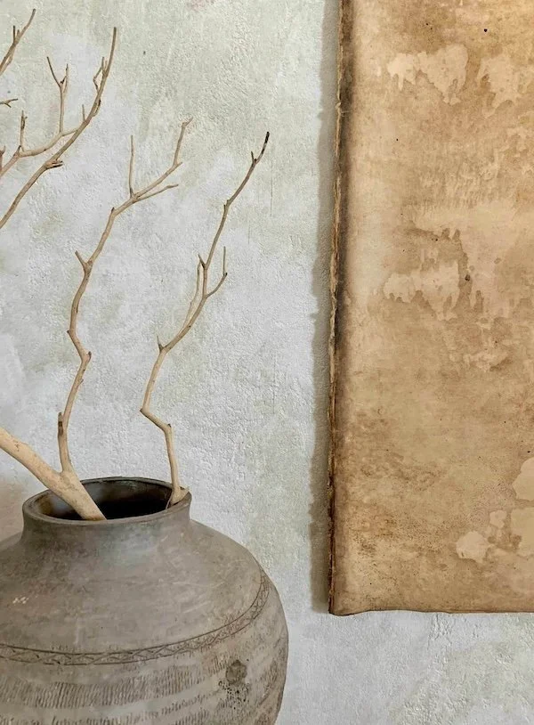 A large, textured ceramic vase with leafless branches next to a textured wall with a vertical strip of plain wall on the right.