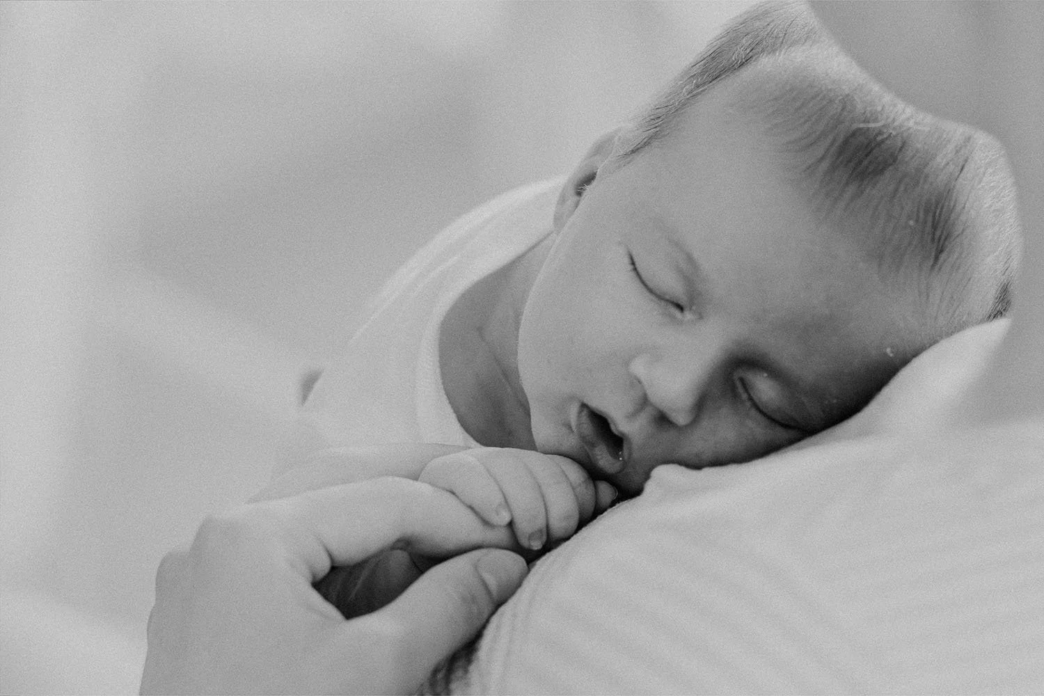 Søvnende baby med hendene sammen, liggende på en pute, i svart-hvitt.