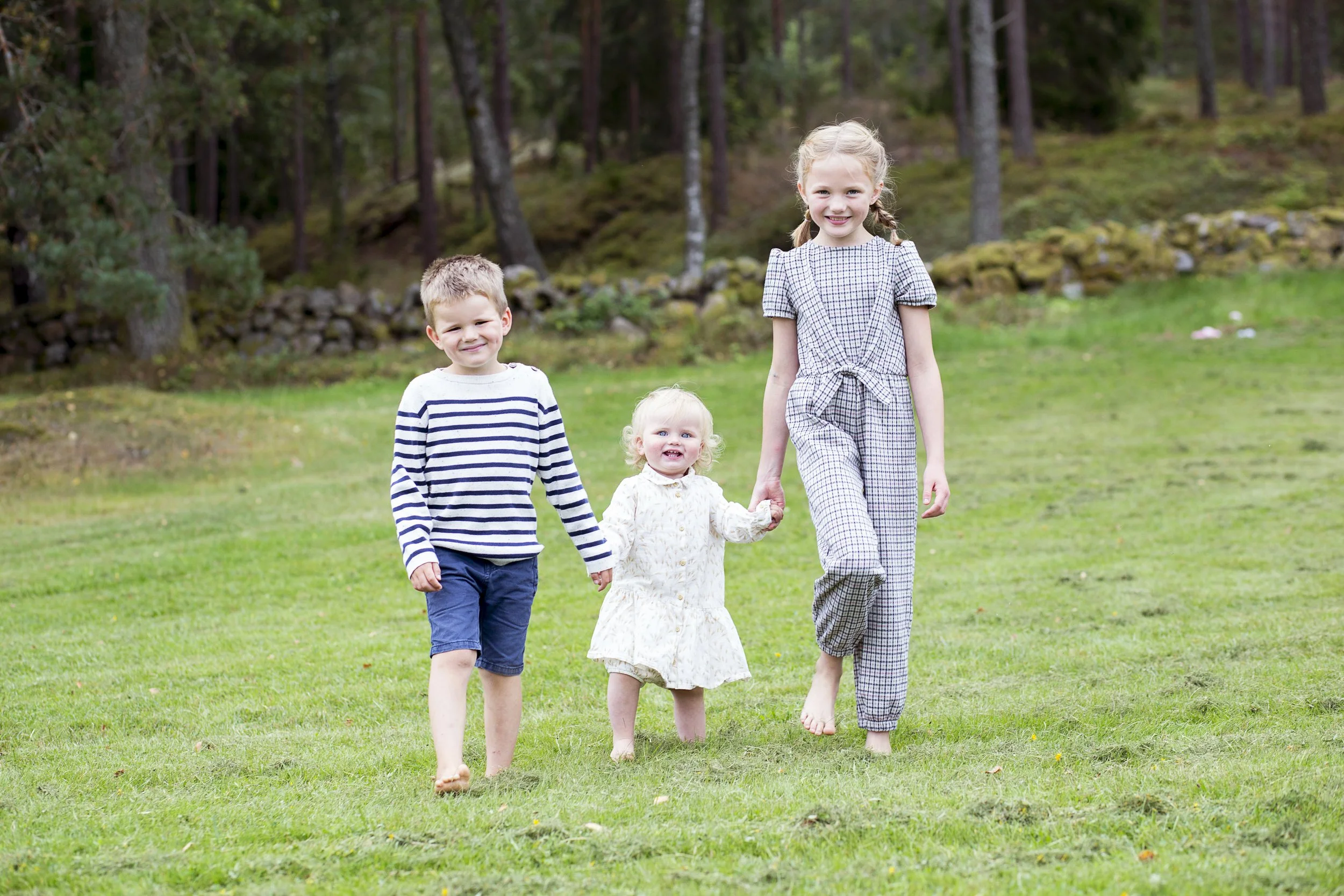 Fire barn og en unge jente som går på gressplen i en skog.