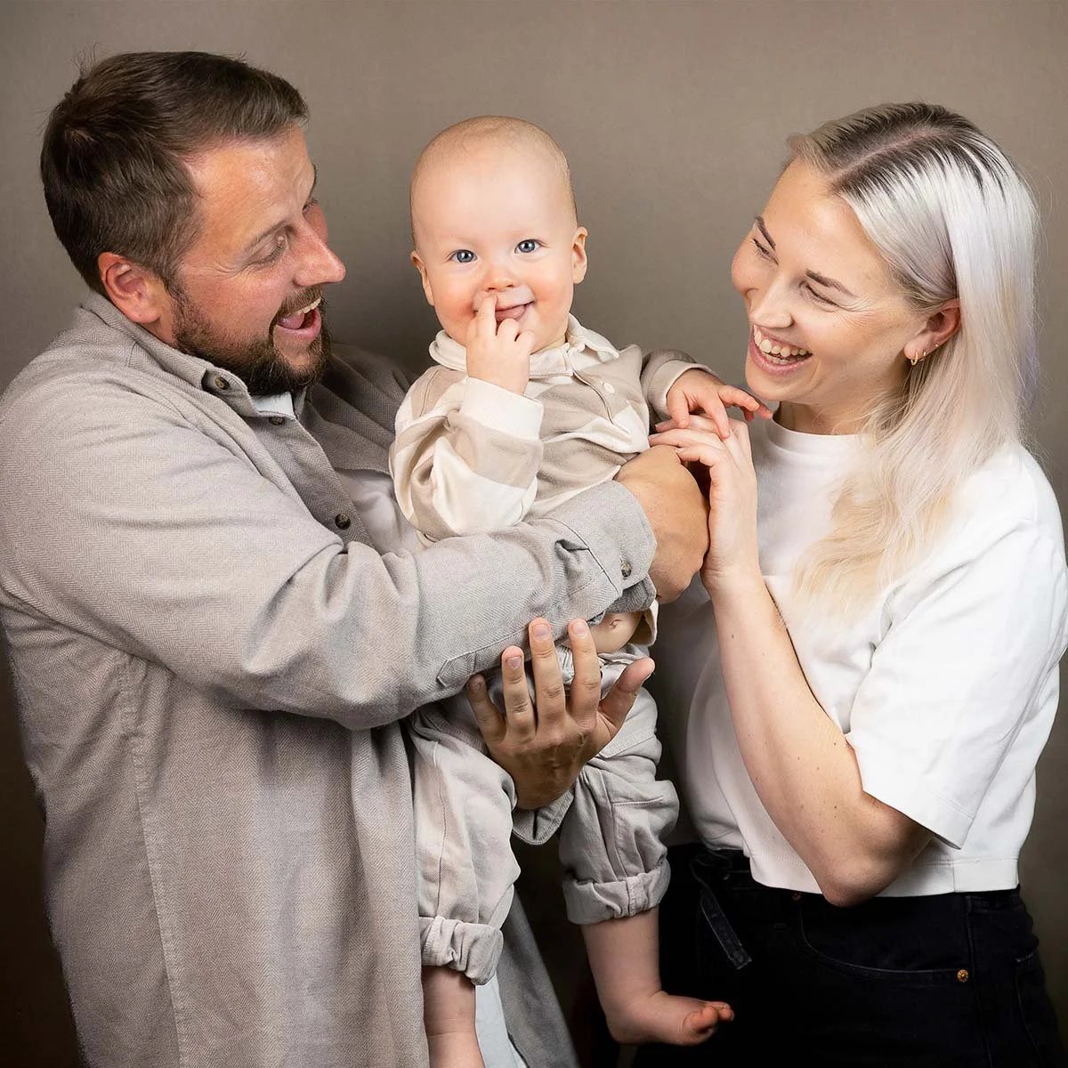 Et lykkelig familie med en far, mor og liten baby som smiler og ler, bader i kjærlighet og glede.