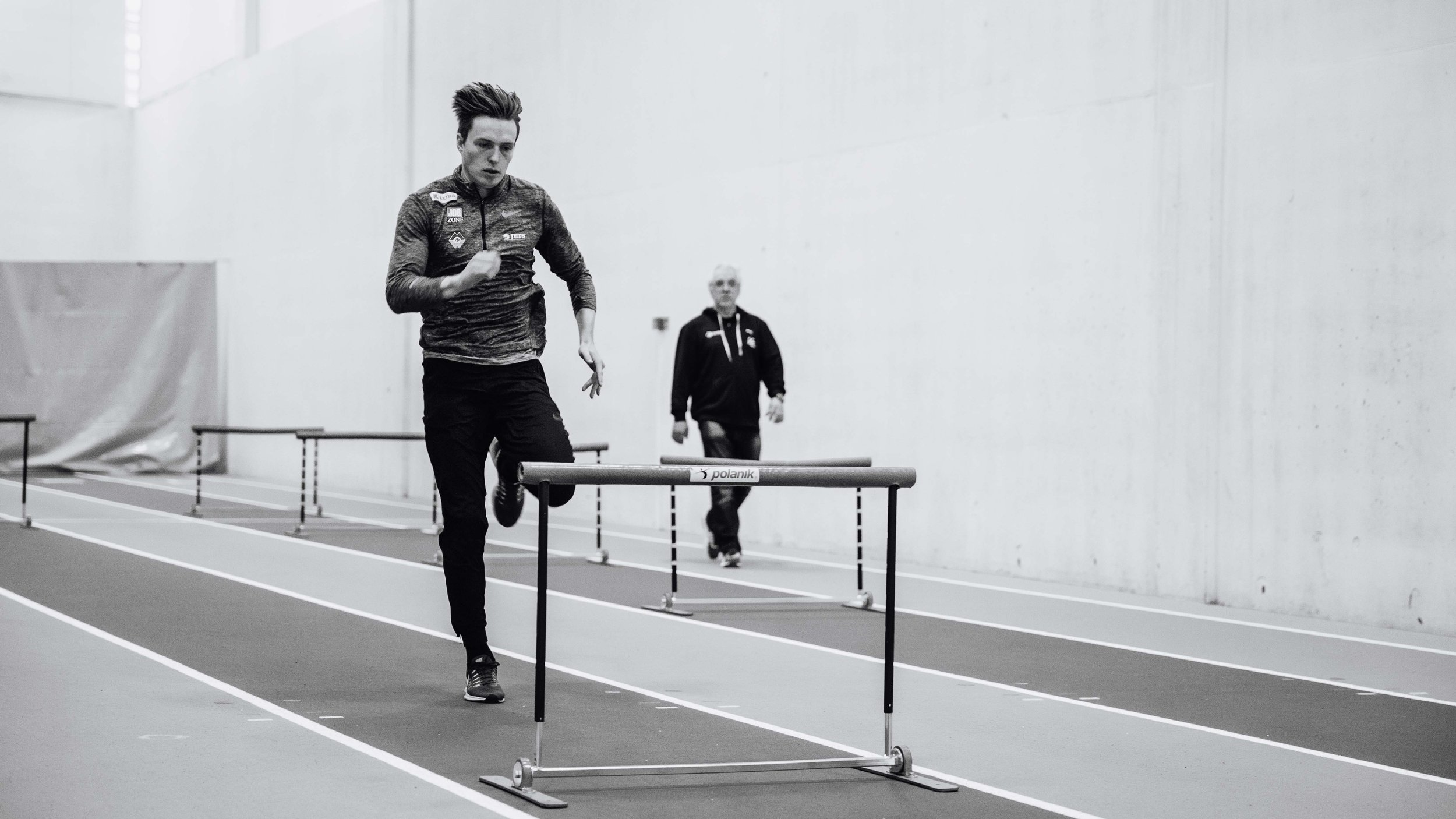 To personer deltar i innendørs hekketraining; en person hopper over en hekk, mens den andre følger bak.