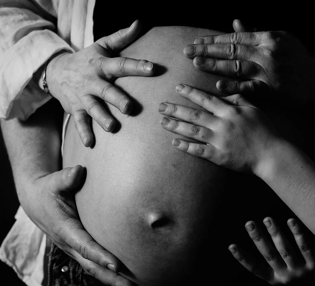 Seks personer som holder rundt en gravid mage, med hendene plassert rundt den.
