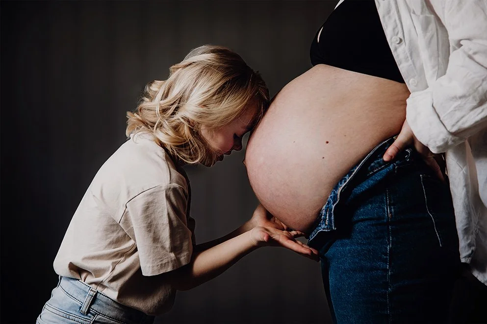 En ung jente som kysser en gravid kvinnes mage.