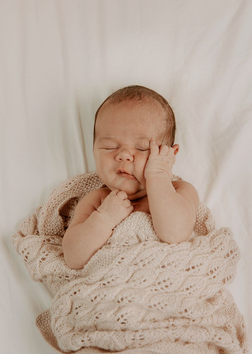 Søvnende baby som ligger innpakket i et mykt klesplagg på en seng.