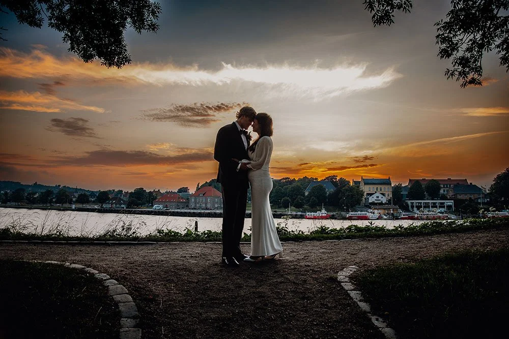 Et romantisk bilde av en brudepar som står ansikt til ansikt under en solnedgang i Gamlebyen i Fredrikstad. Bildet er tatt av Vatafoto, som er en erfaren bryllupsfotograf i Fredrikstad