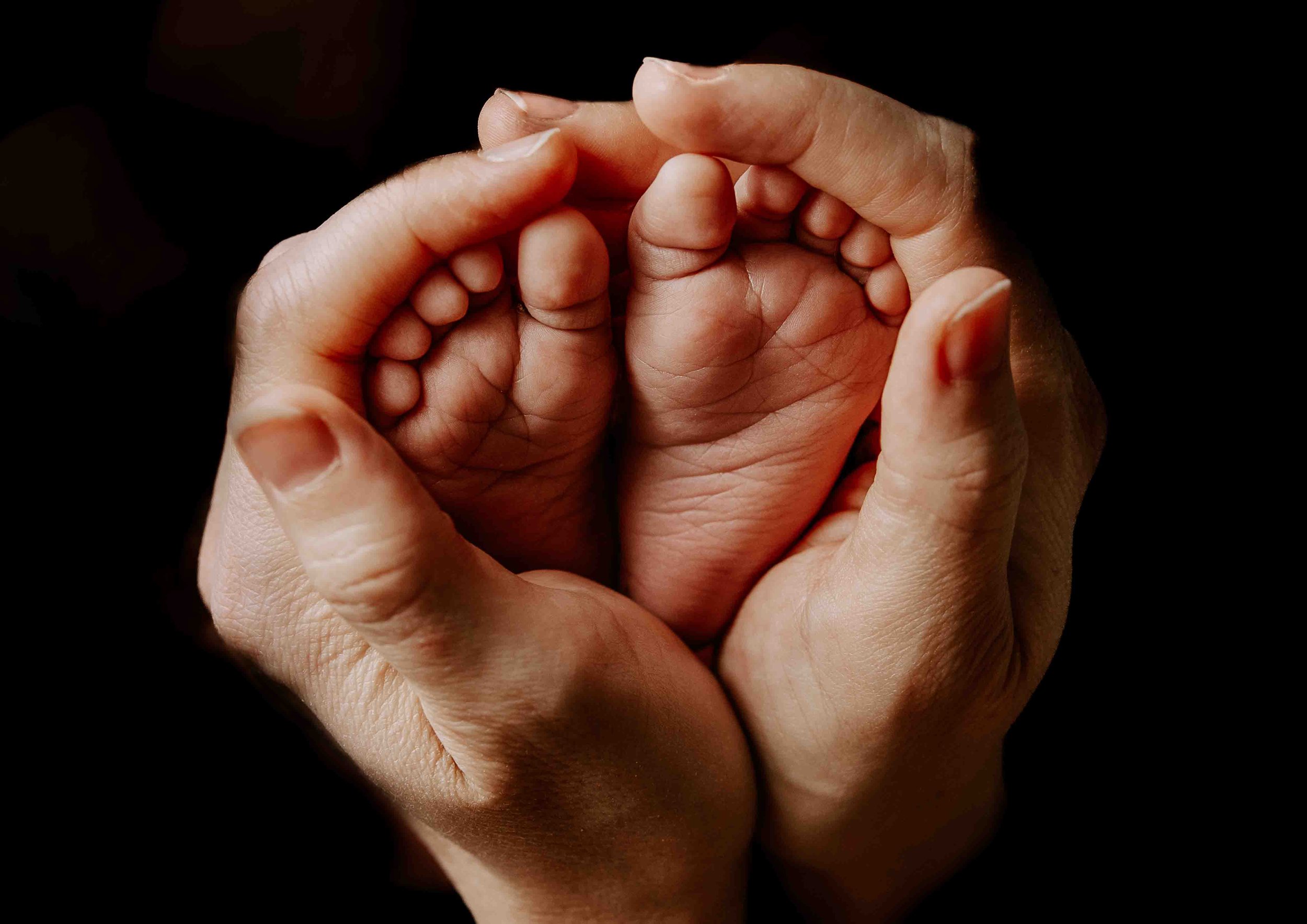 To voksne hender holder en liten babyhånd, symbol på omsorg og beskyttelse.