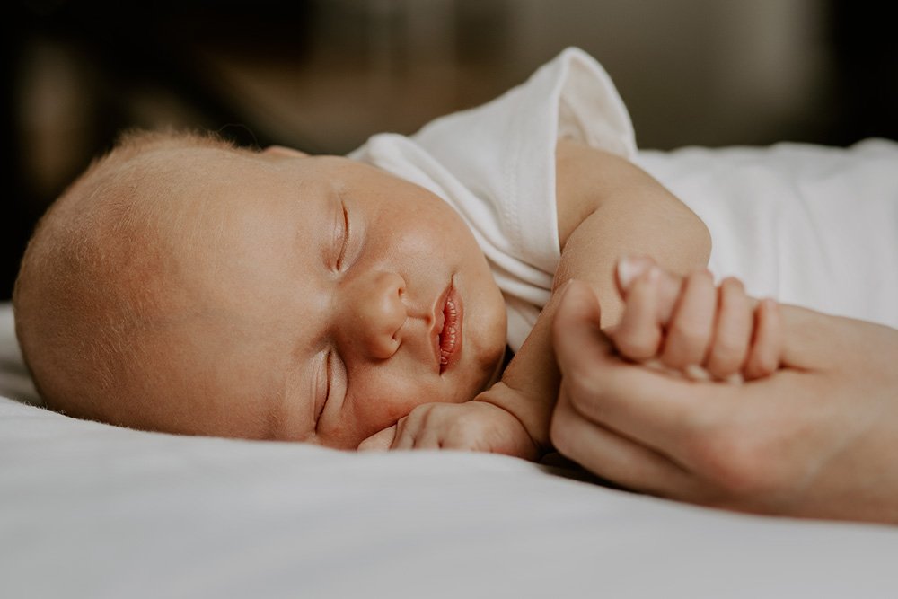 En sovende baby som holder mors finger. Det er et eksempel på et bilde som er tatt under en nyfødtfotografering hjemme hos en kunde. Bildet er tatt av vatafoto.