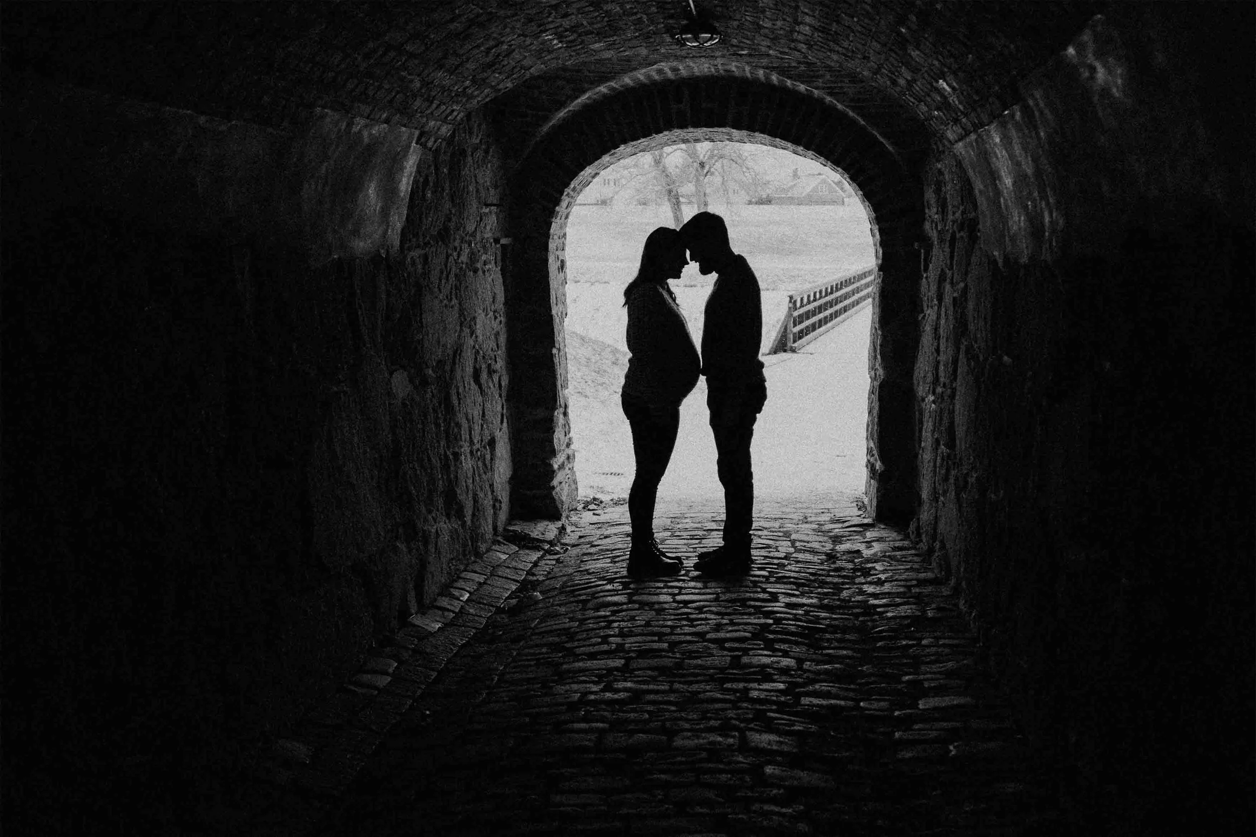 To personer som står ansikt mot ansikt under en tunnel, med pannen berøring, og et landskap i bakgrunnen.