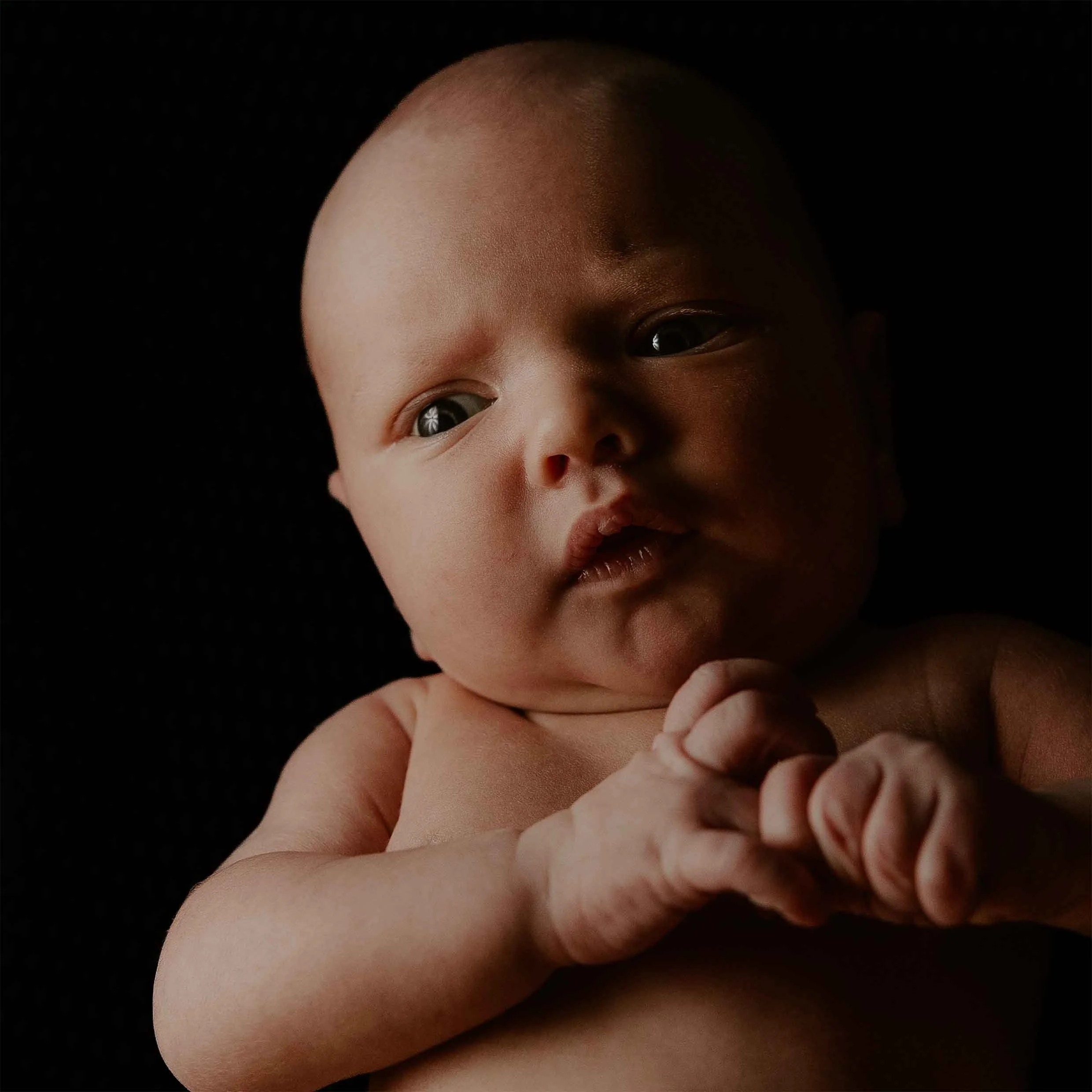 Nærbilde av en sovende baby med lys hud, uten klær, på en svart bakgrunn.