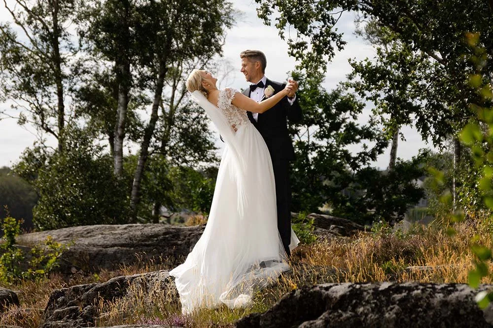Et brudepar i bryllupskledig danse ute i naturen.