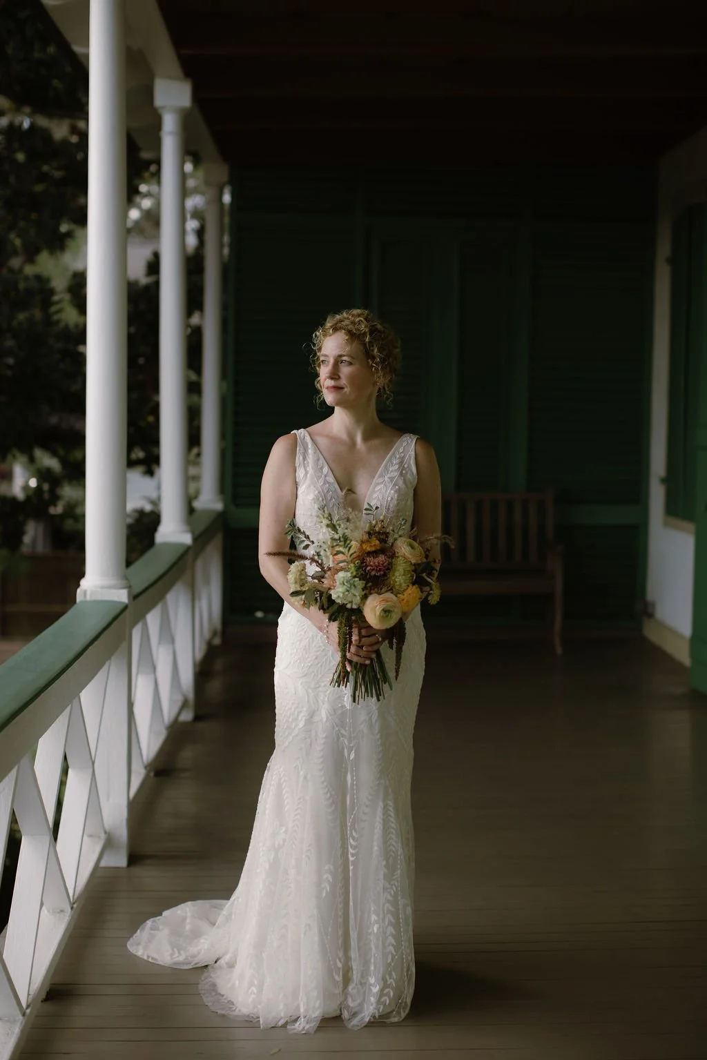 Woman wearing a white bridal dress and holding a bouquet standing on a balcony