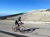A child riding a bicycle on a mountain road with scenic mountains and blue sky in the background.