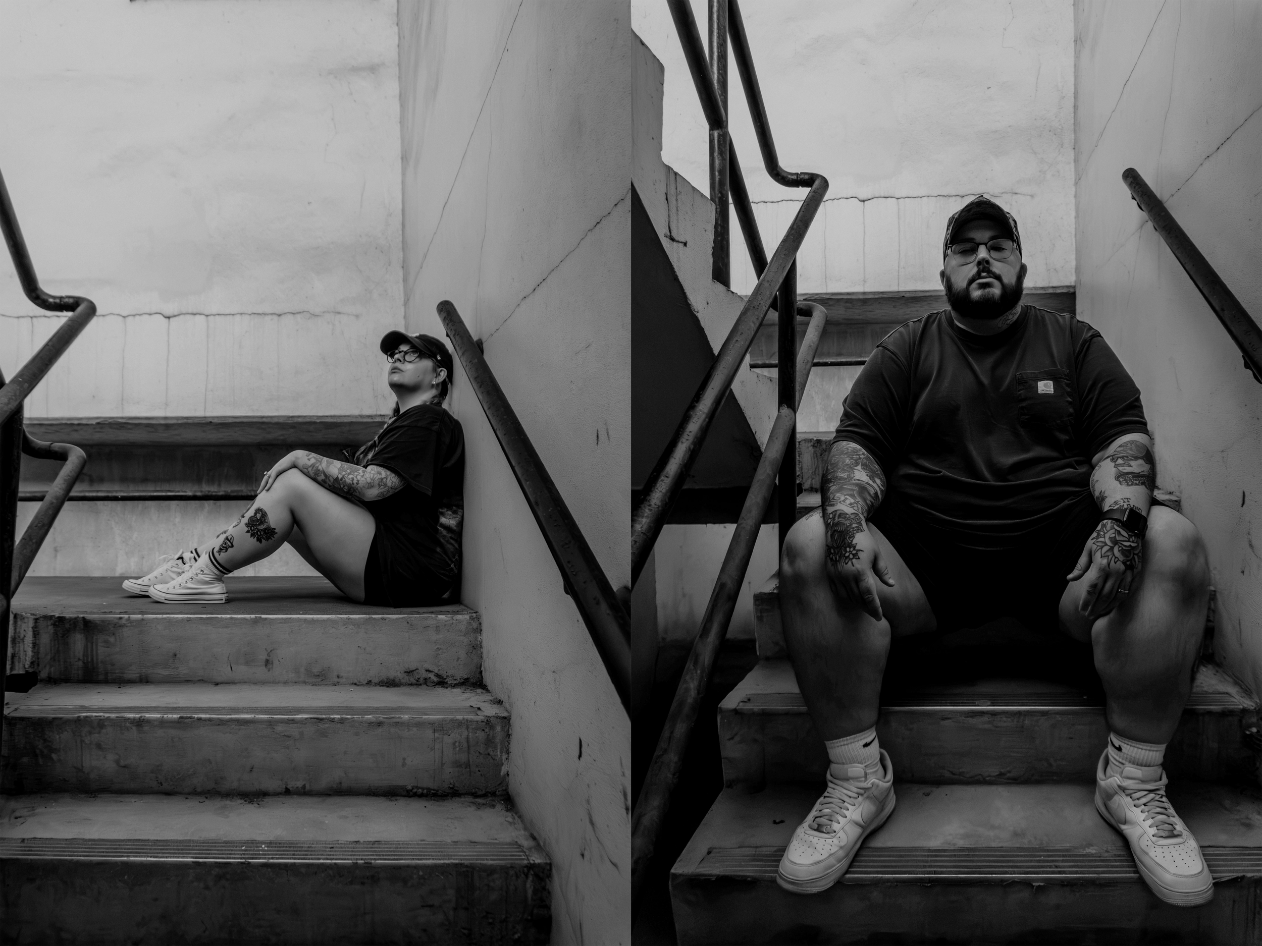 A black and white photo of a woman sitting on the stairs, wearing glasses, a cap, and casual clothes, with tattoos on her arms and legs. Next to her, a man is sitting on the stairs, also with tattoos, wearing glasses, a cap, a dark t-shirt, and sneakers.