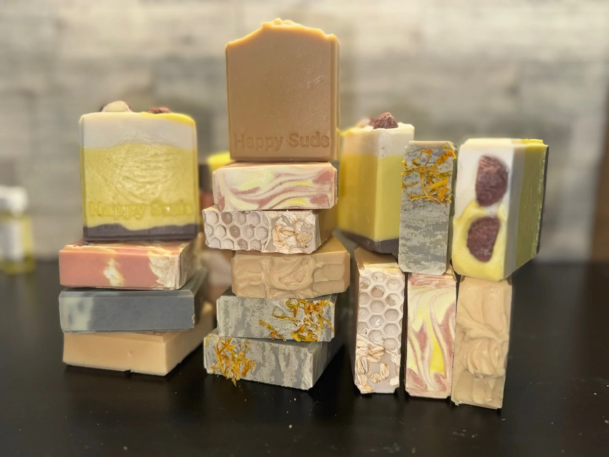 An assortment of handmade soap bars with different colors, textures, and patterns, arranged in stacks on a dark surface.