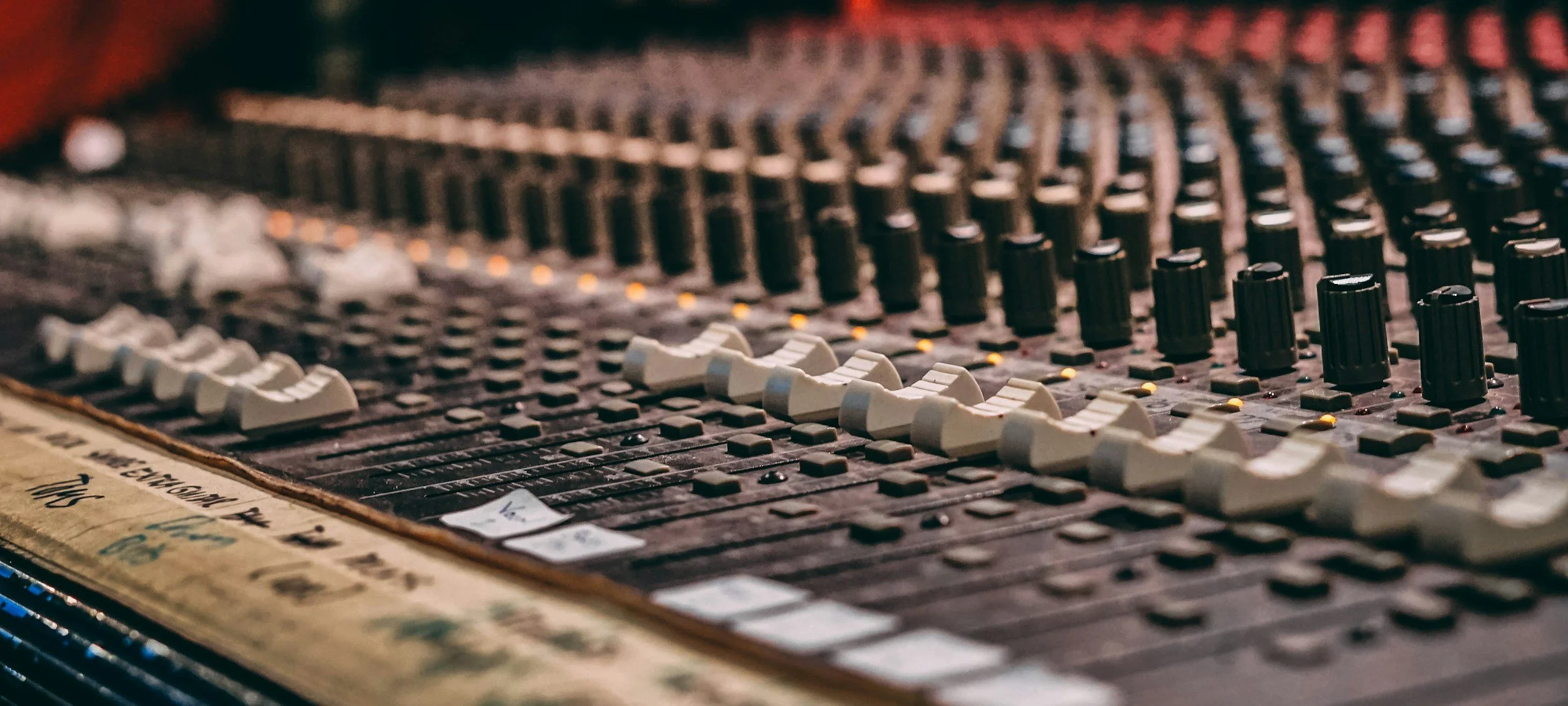 Close-up of a professional audio mixing console with multiple white and black knobs and sliders adjusting sound levels.
