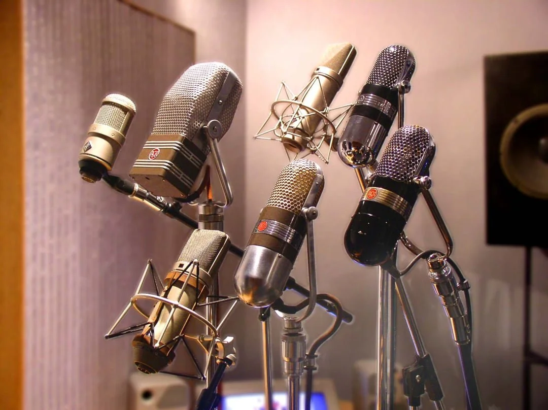 A collection of vintage microphones on stands in a recording studio.