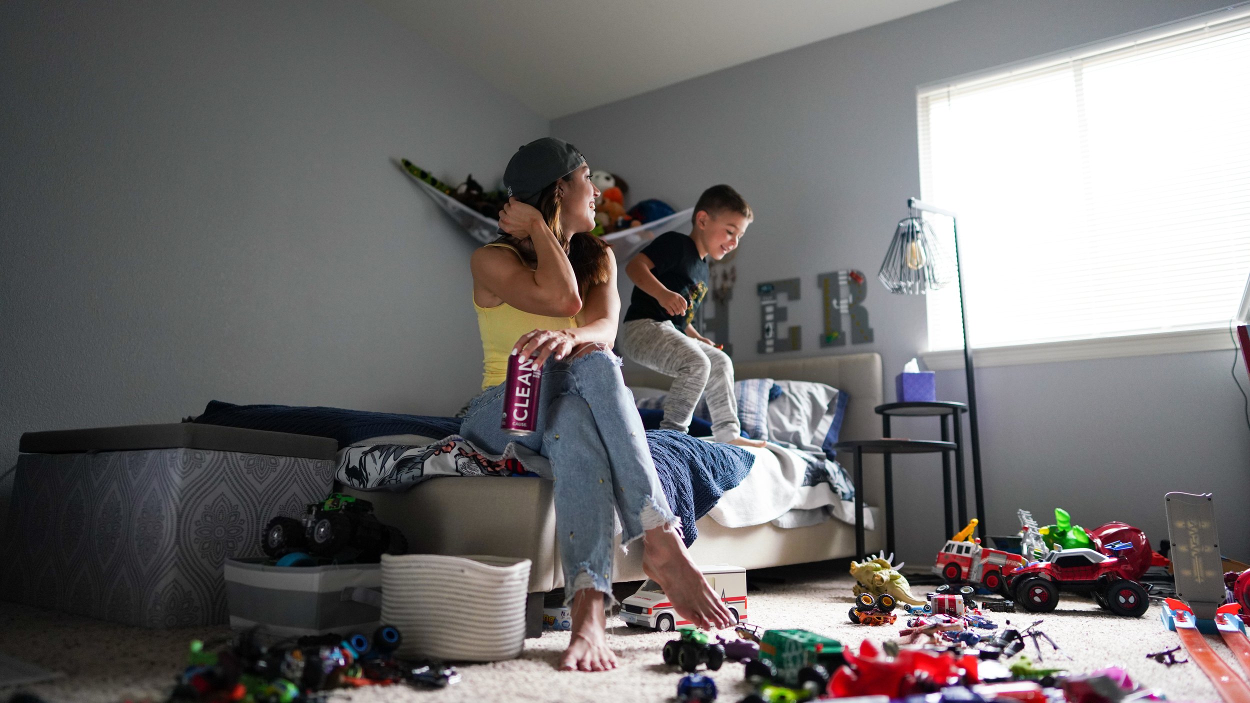 A woman and a young boy playing with toy cars on the floor in a bedroom.