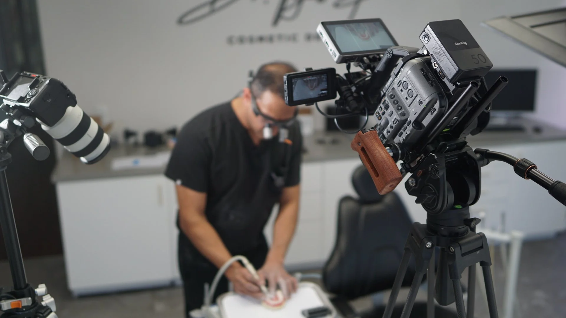 A professional camera on a tripod is filming a person performing a science experiment or demonstration in a modern office or studio setting.