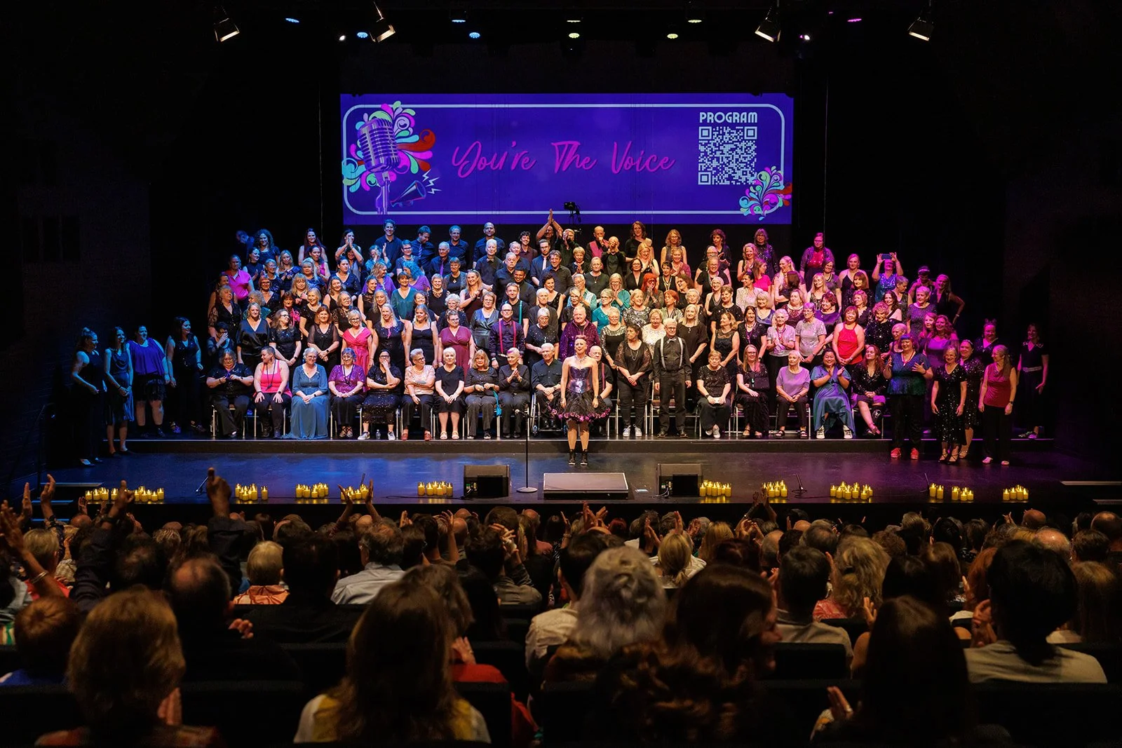 Choir in an auditorium with the crowd celebrating and clapping for an encore