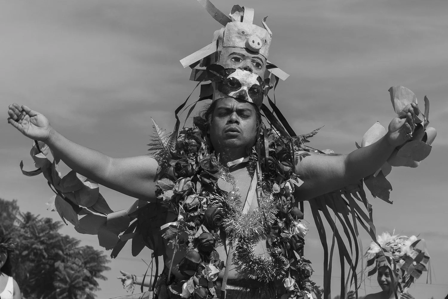 Persona participando en un festival cultural con disfraz tradicional y decoraciones de hojas y flores.
