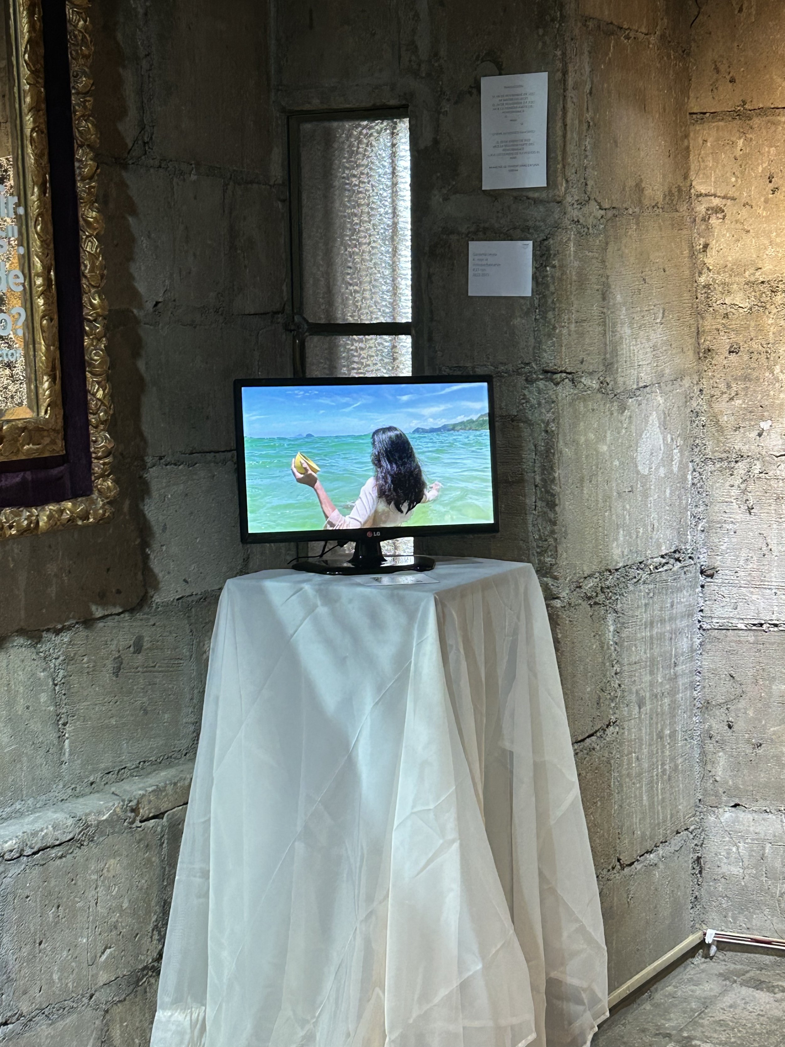 Pantalla sobre una mesa cubierta con tela blanca, muestra a persona en playa.