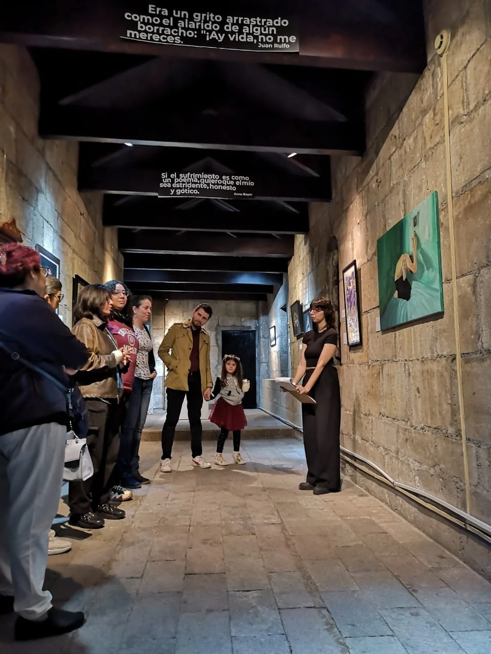 Grupo de personas en una galería de arte con cuadros en las paredes y citas literarias en el techo.