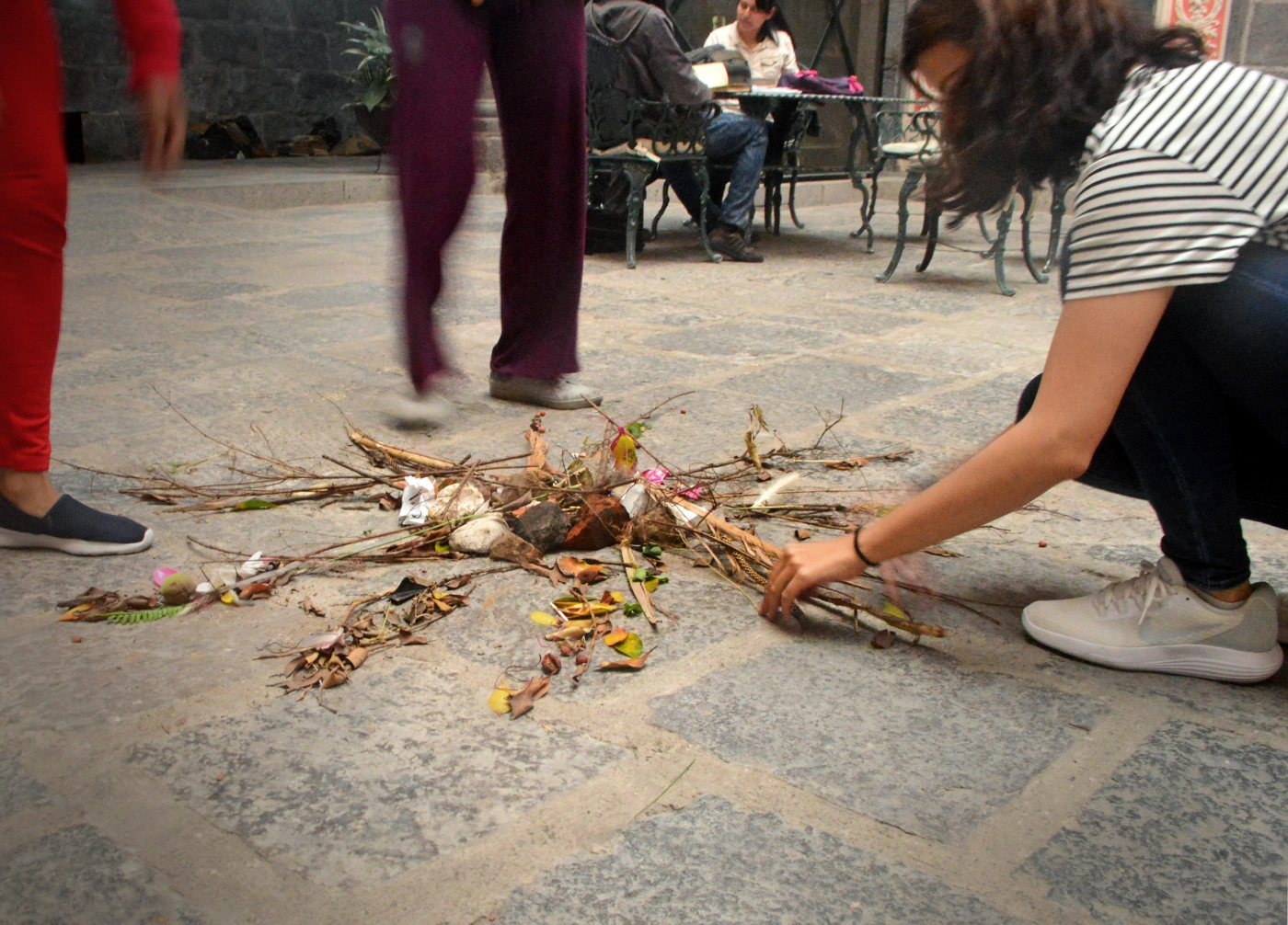 Personas creando un mandala de ramas y hojas en el suelo, dentro de un espacio interior con mesas y sillas.