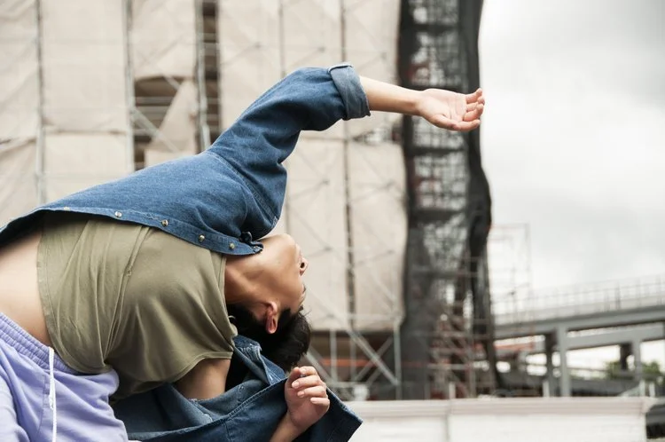 Persona realizando una postura de danza acrobática con un fondo de estructura tipo andamio.