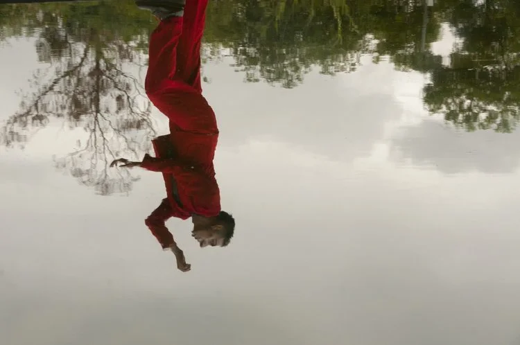 Reflejo de una persona corriendo vestida de rojo en el agua, con árboles alrededor.