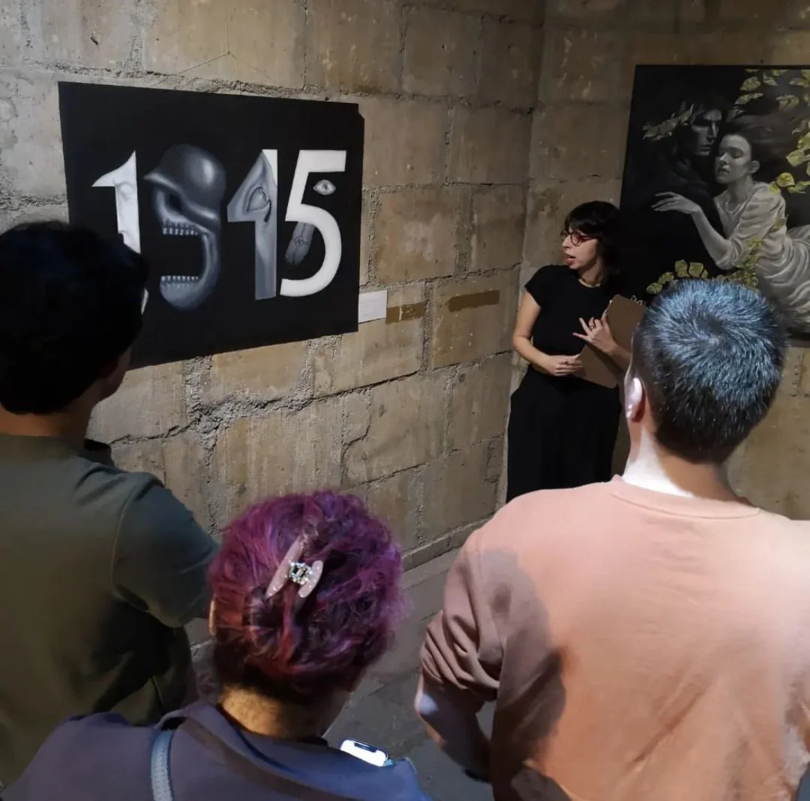 Personas observan una obra de arte numerada en una pared de concreto en una galería. Hay una guía explicando la obra.