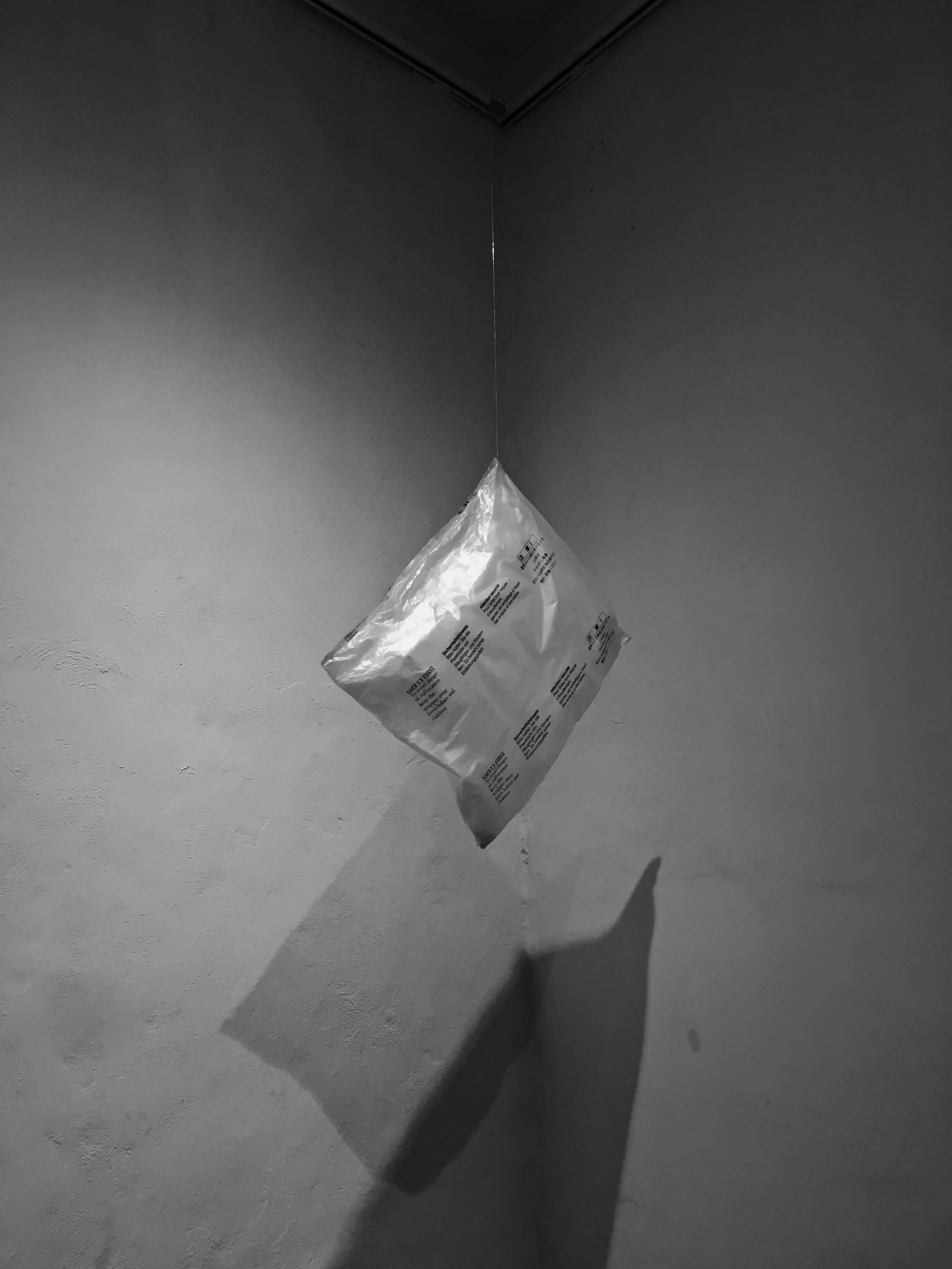 Una bolsa de plástico con texto colgando en una esquina de una habitación, proyectando una sombra en la pared.