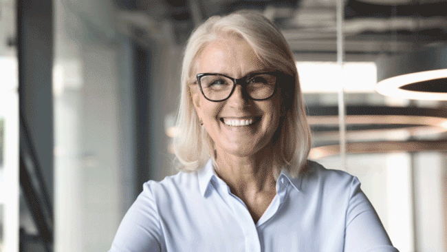 Middle-aged woman with blonde hair and black glasses smiling in an office setting. Lower thirds of a melting cheese with the presenter name and title builds on and off the screen.