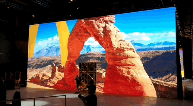 Large digital screen display showing a desert landscape with red rock formations, blue sky, and distant mountains, featuring McDonald's Golden Arches.
