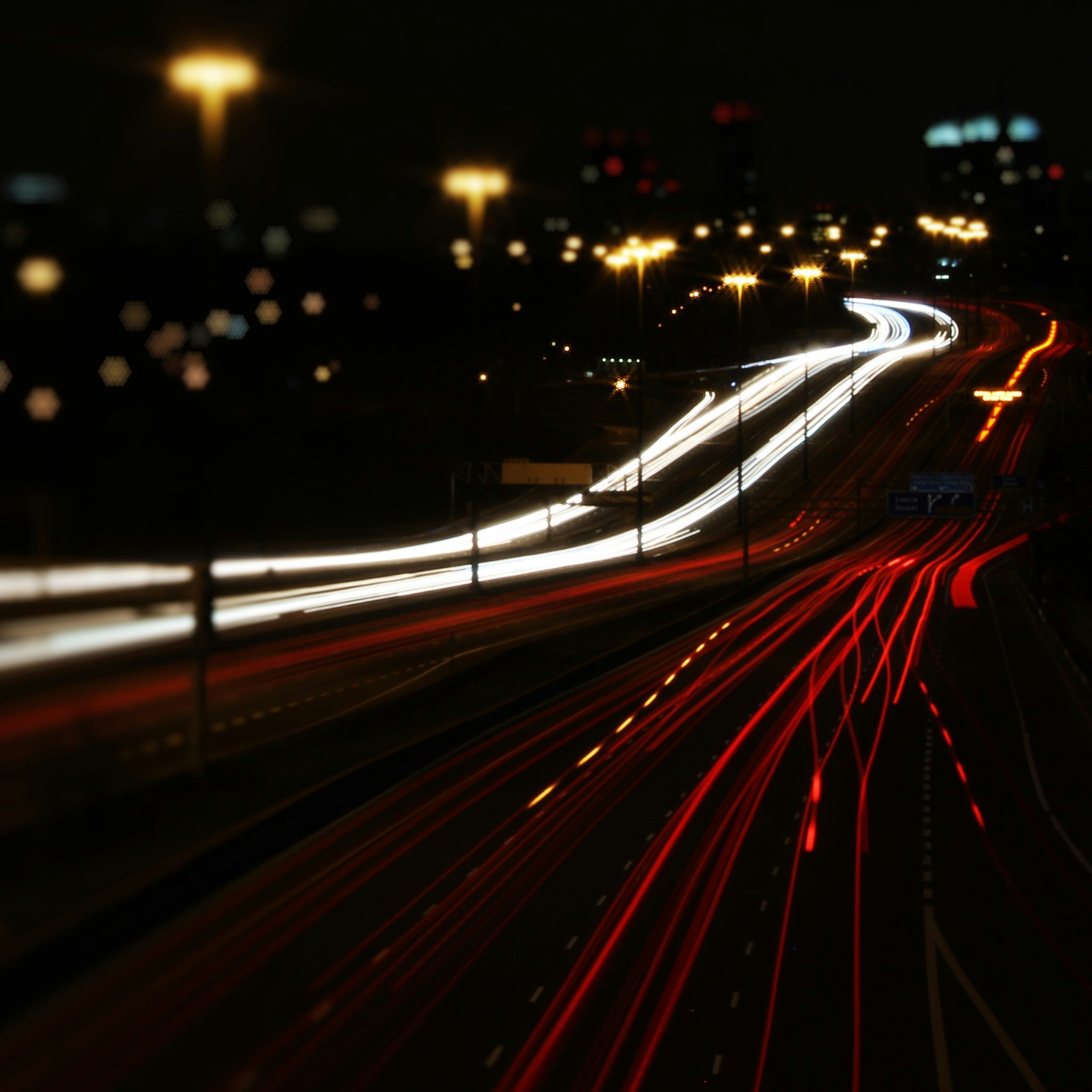 Nighttime view of a highway with moving vehicle light trails in white and red, and illuminated streetlights.