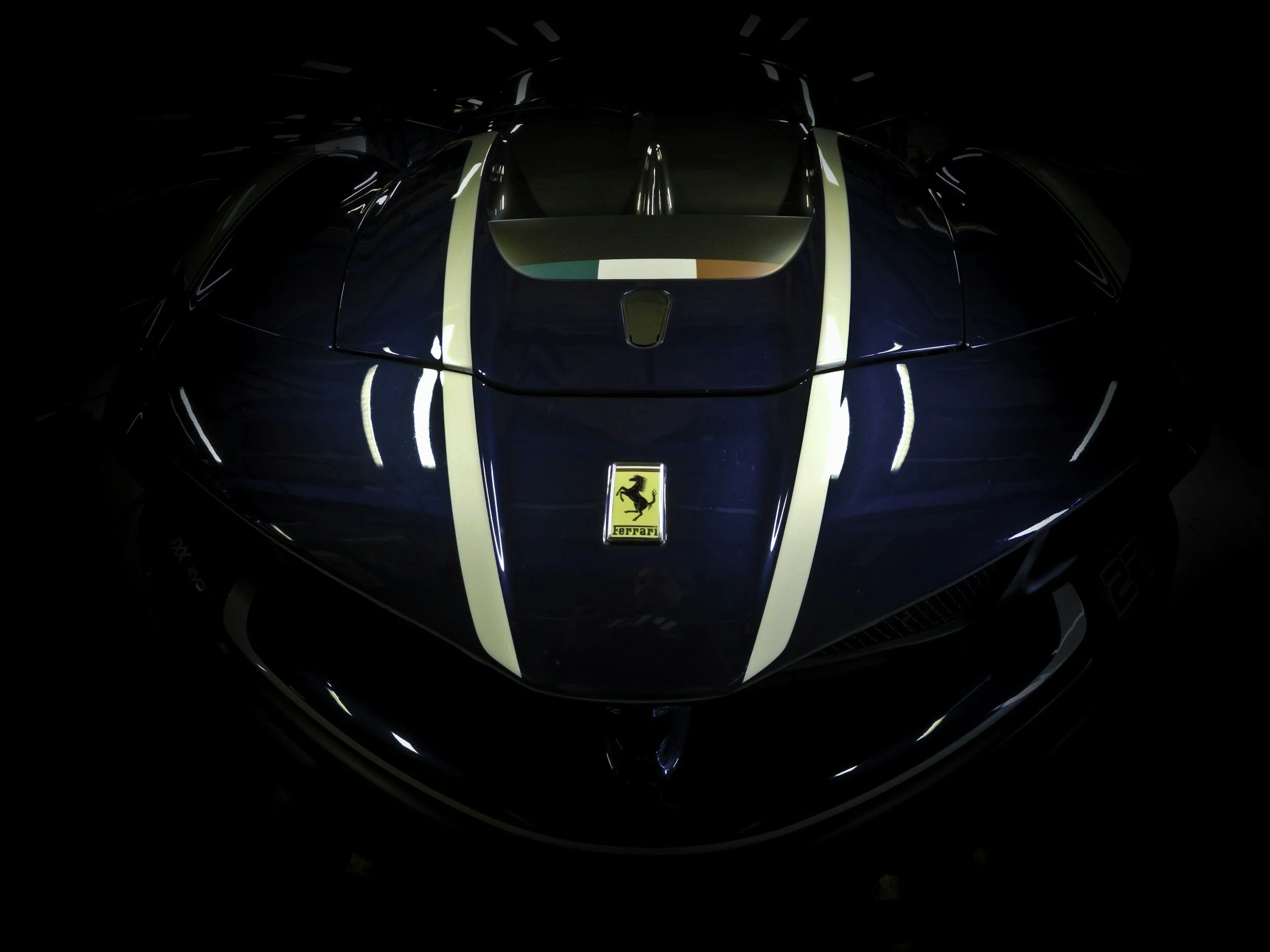 Top view of a dark blue Ferrari sports car with white racing stripes and an Italian flag decal on the hood, showcasing its sleek design and logo.
