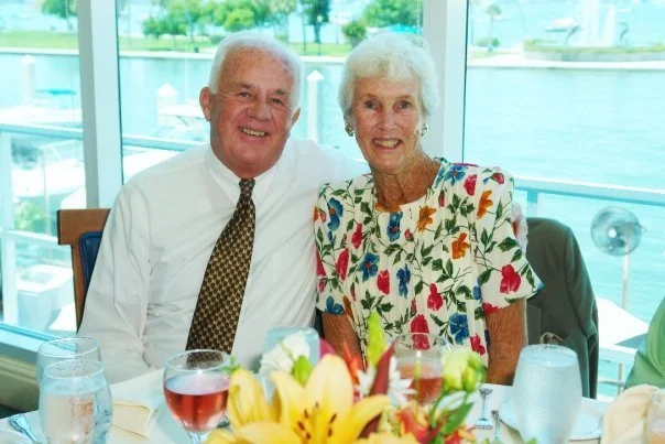 Couple smiling for photo with water and marina behind them