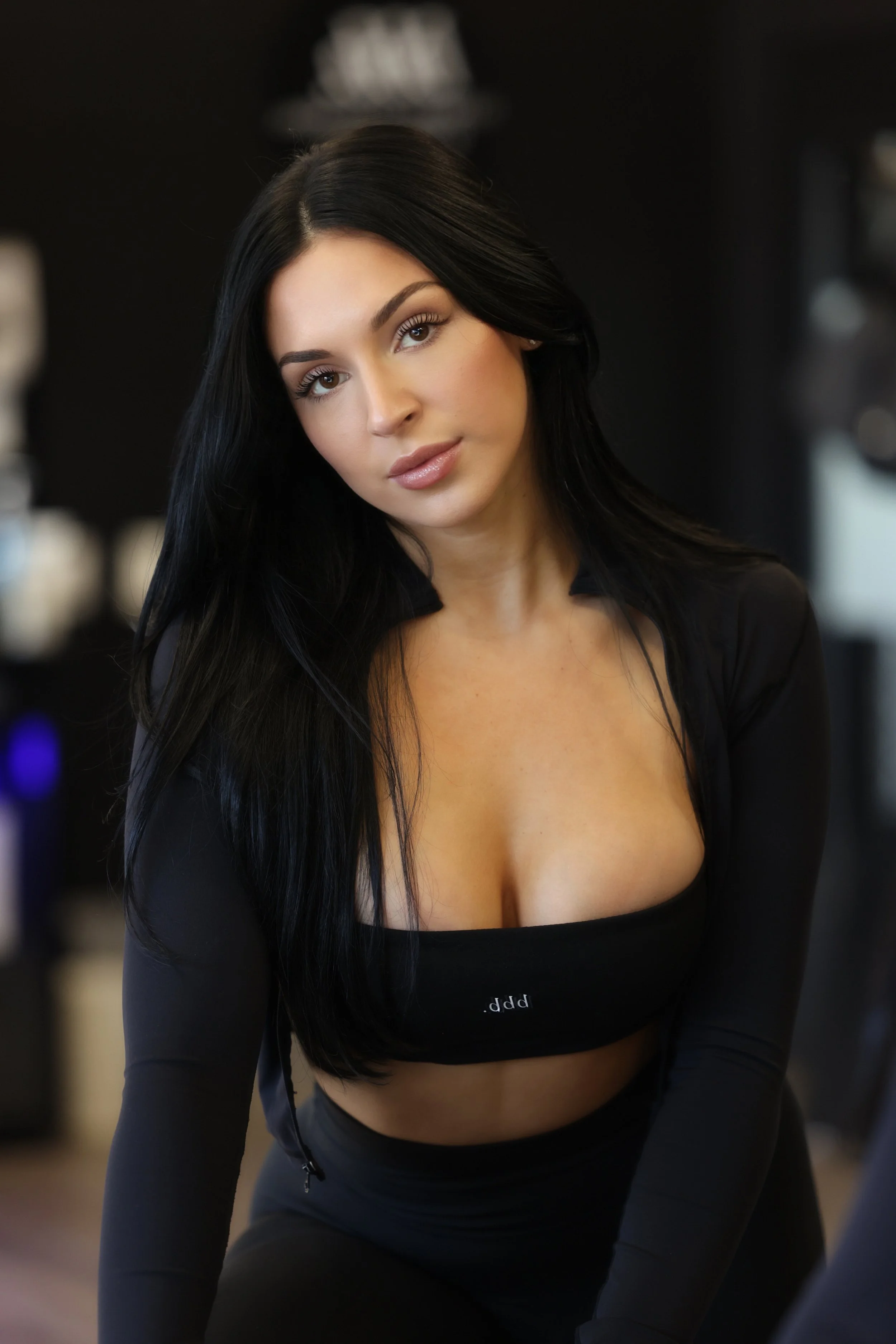 A woman with long black hair, tan skin, and wearing a black top and jacket, looking into the camera.