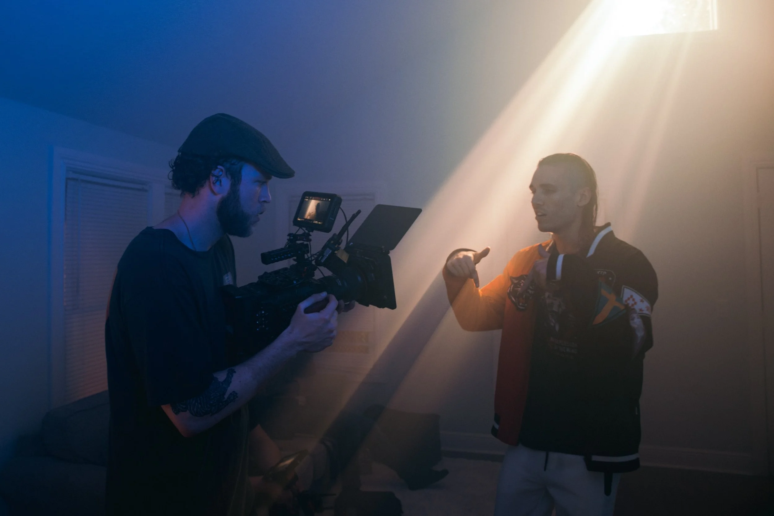Cameraman filming a person in a dimly lit room with light beams.