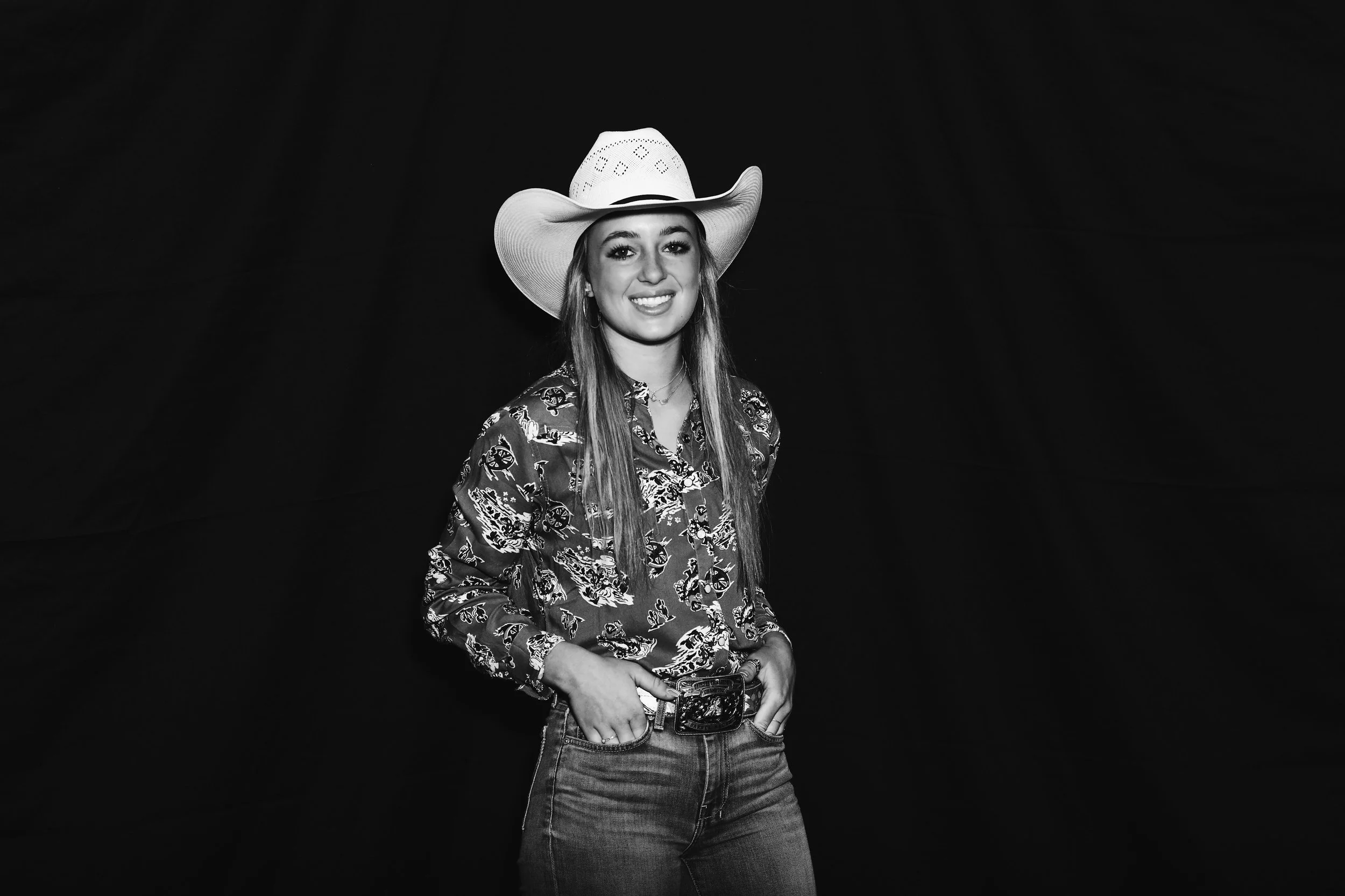 Young woman in a cowboy hat and plaid shirt, smiling against a black background.