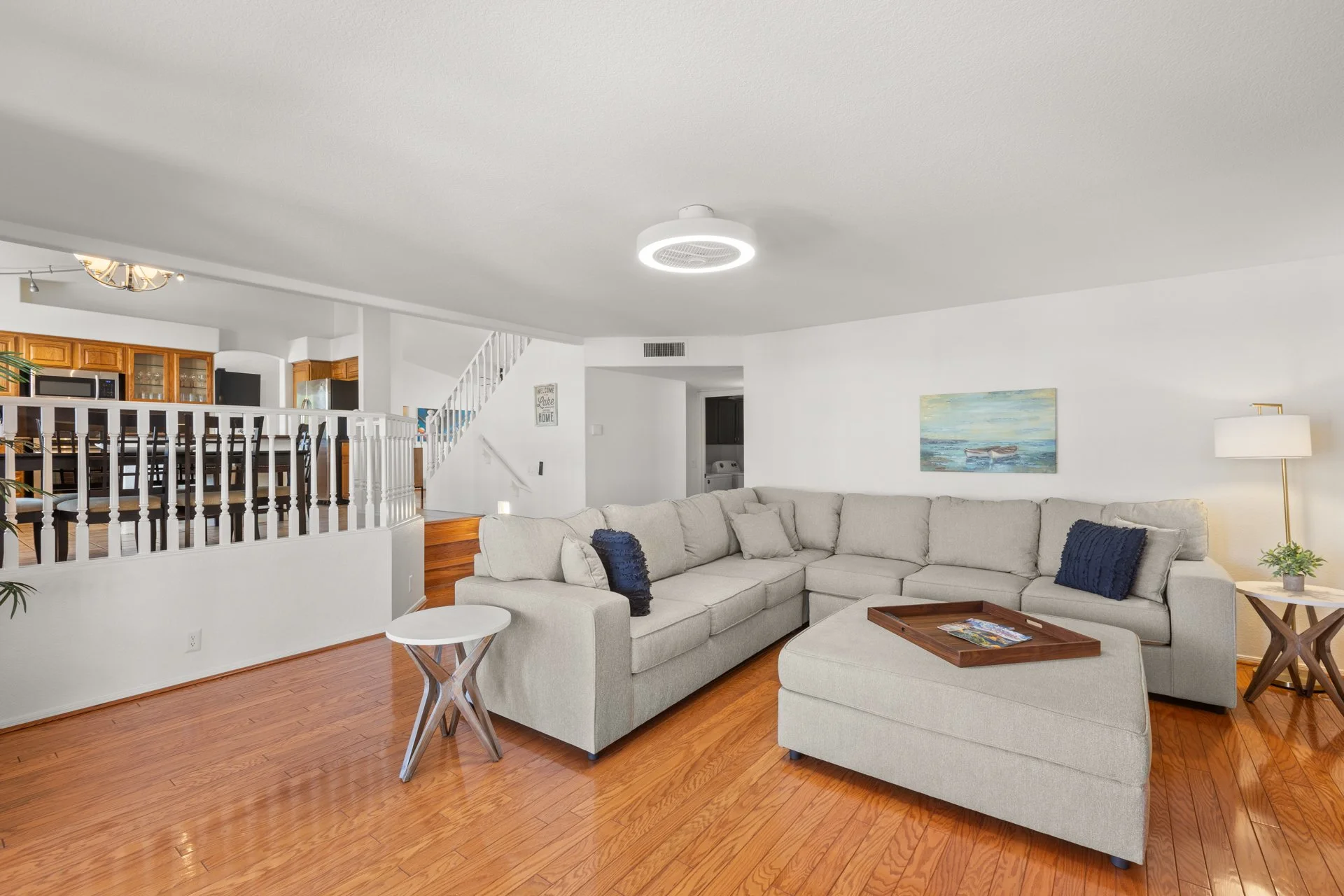 Living room with beige sectional sofa, wooden coffee table, artwork on white wall, and hardwood floors.