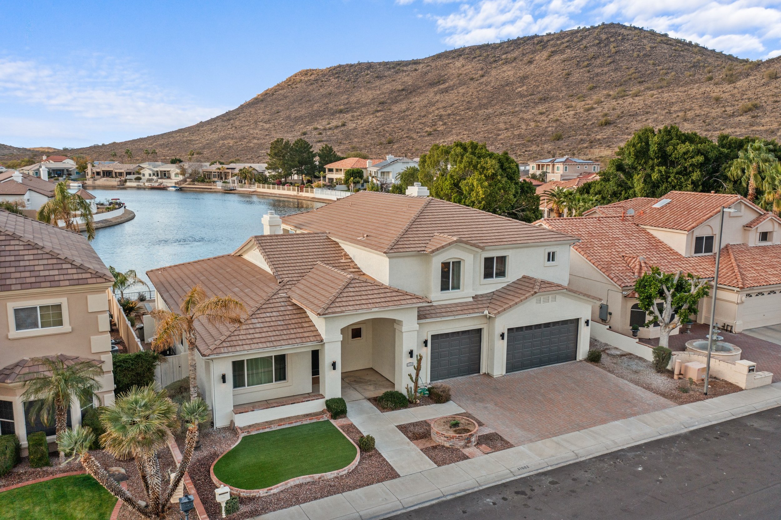 A suburban neighborhood with houses, a waterway, and a hillside background under a partly cloudy sky.