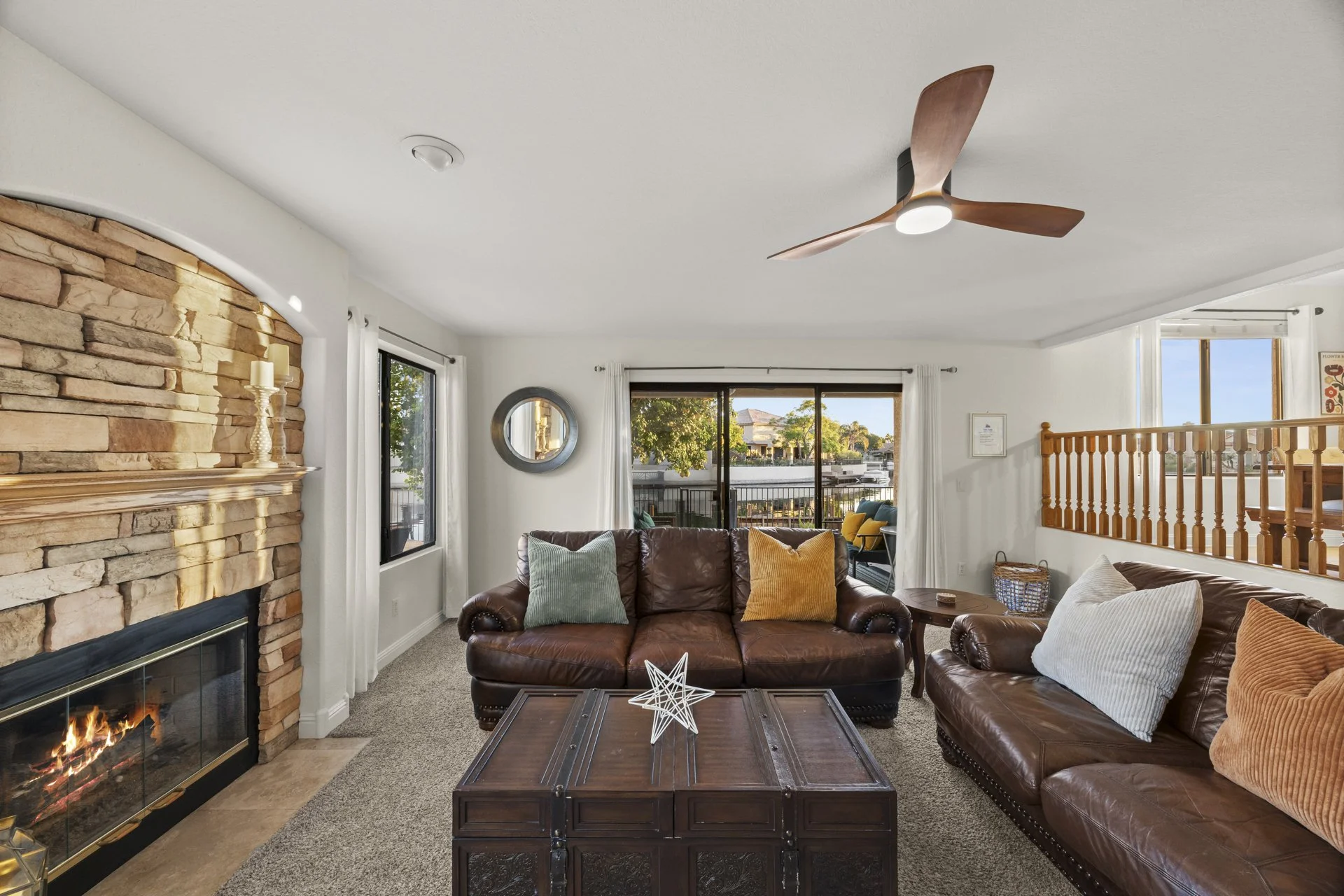 Living room with fireplace, leather sofas, window views, wooden coffee table, ceiling fan, and decorative pillows.