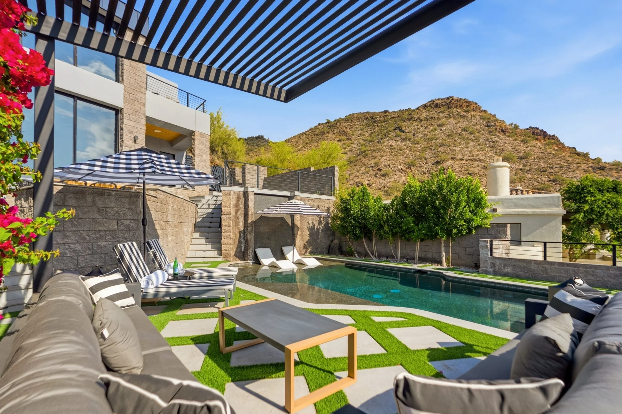 Luxury backyard with modern pool, striped umbrellas, lounge chairs, and mountain view.