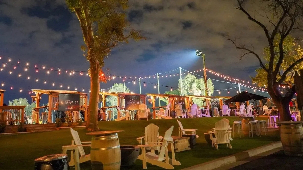 Outdoor seating area with string lights, Adirondack chairs, and food stands at night.