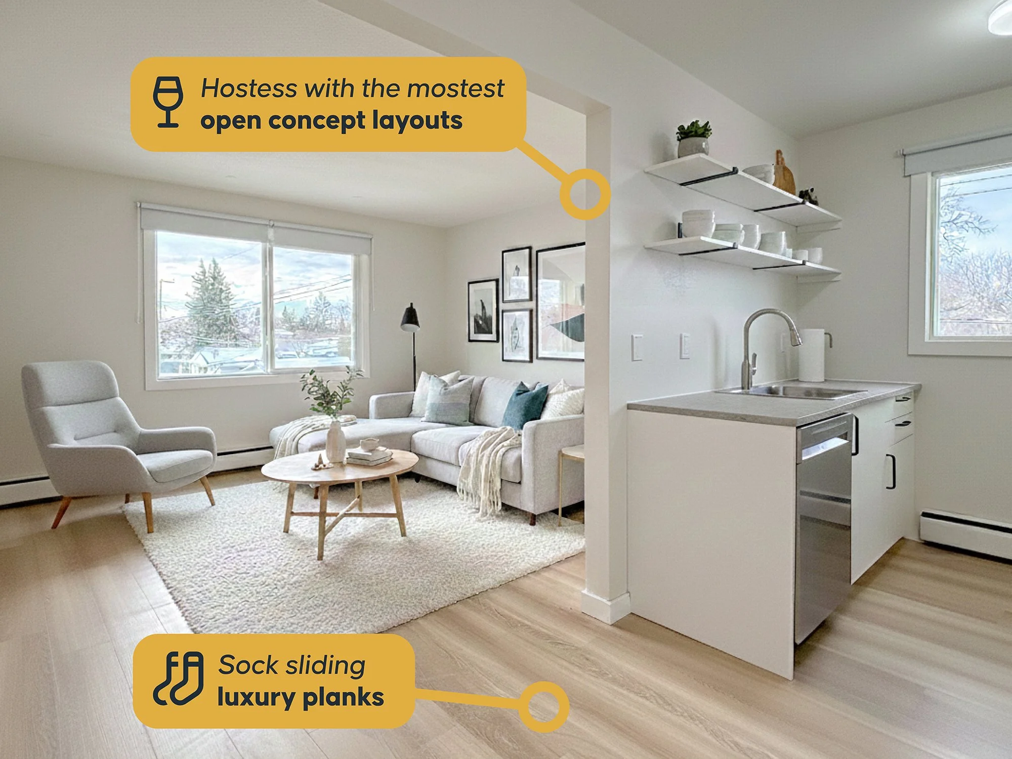 A bright living room and kitchen with large windows, a white sofa with cushions, a modern armchair, a wooden coffee table, and open kitchen shelves with dishes. The room has light wood floors and white walls. Yellow labels highlight the open concept 